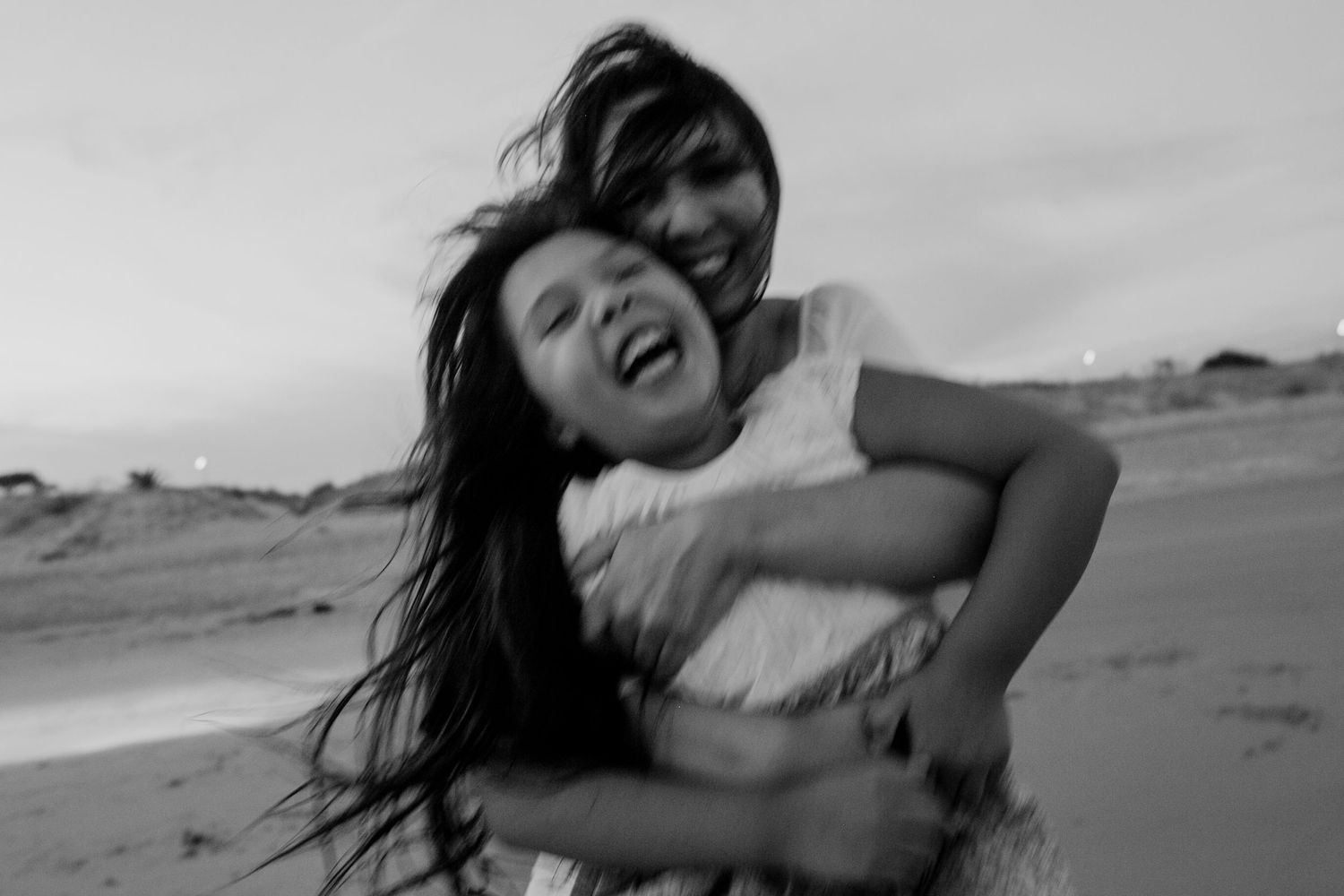A playful black and white capture of two people laughing together on the beach.