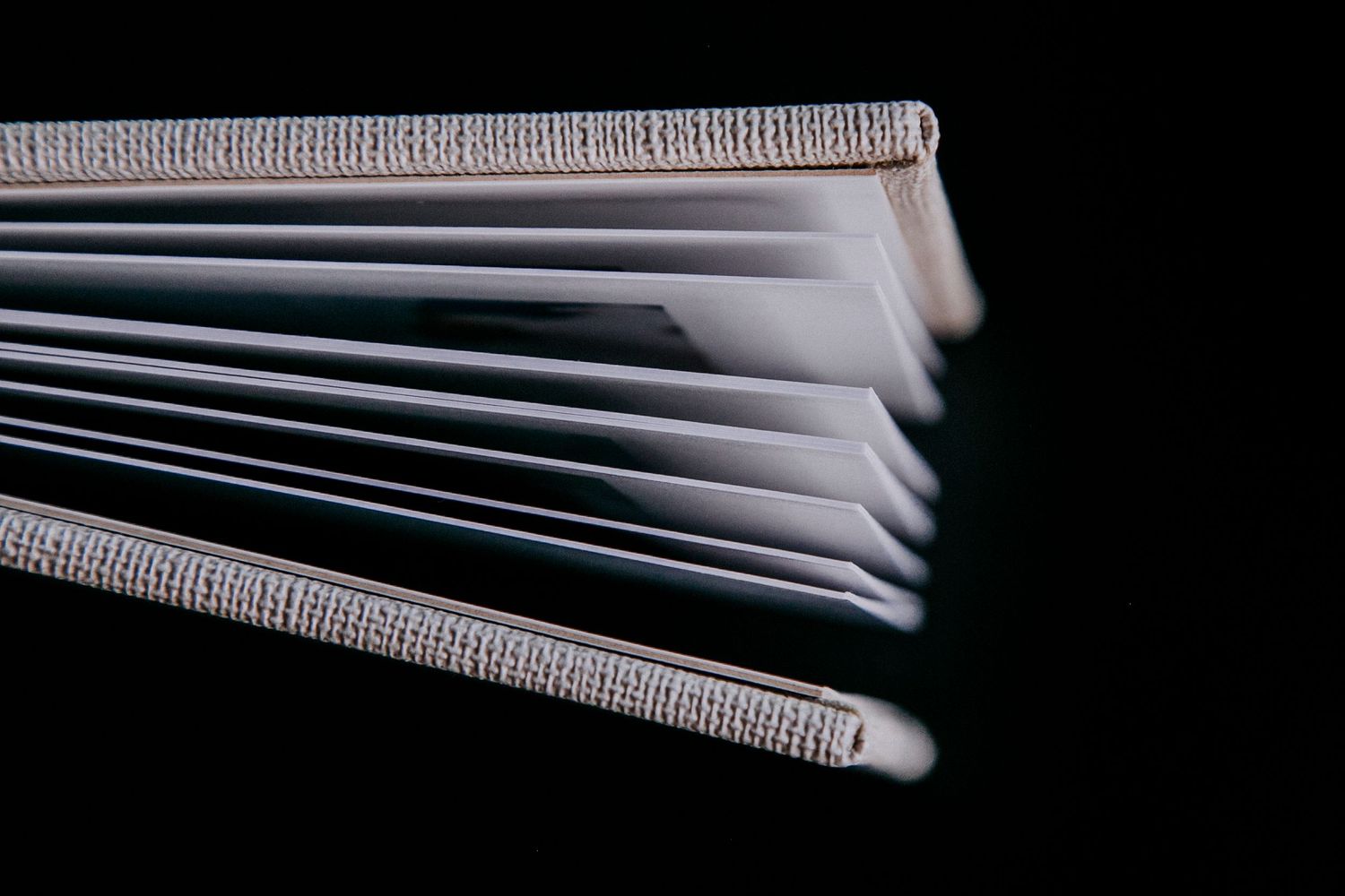 Close-up view of fanned pages in a white hardcover book against dark background.