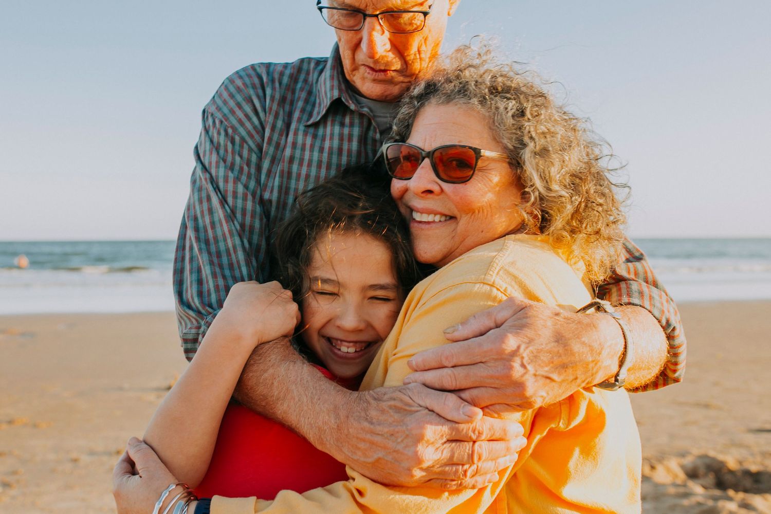 Three people share a tender embrace while enjoying a beautiful day at the beach.