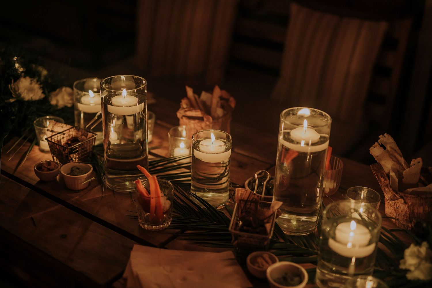 Candlelit mason jars with floating candles and rustic decorations create a warm, romantic atmosphere on a wooden table.
