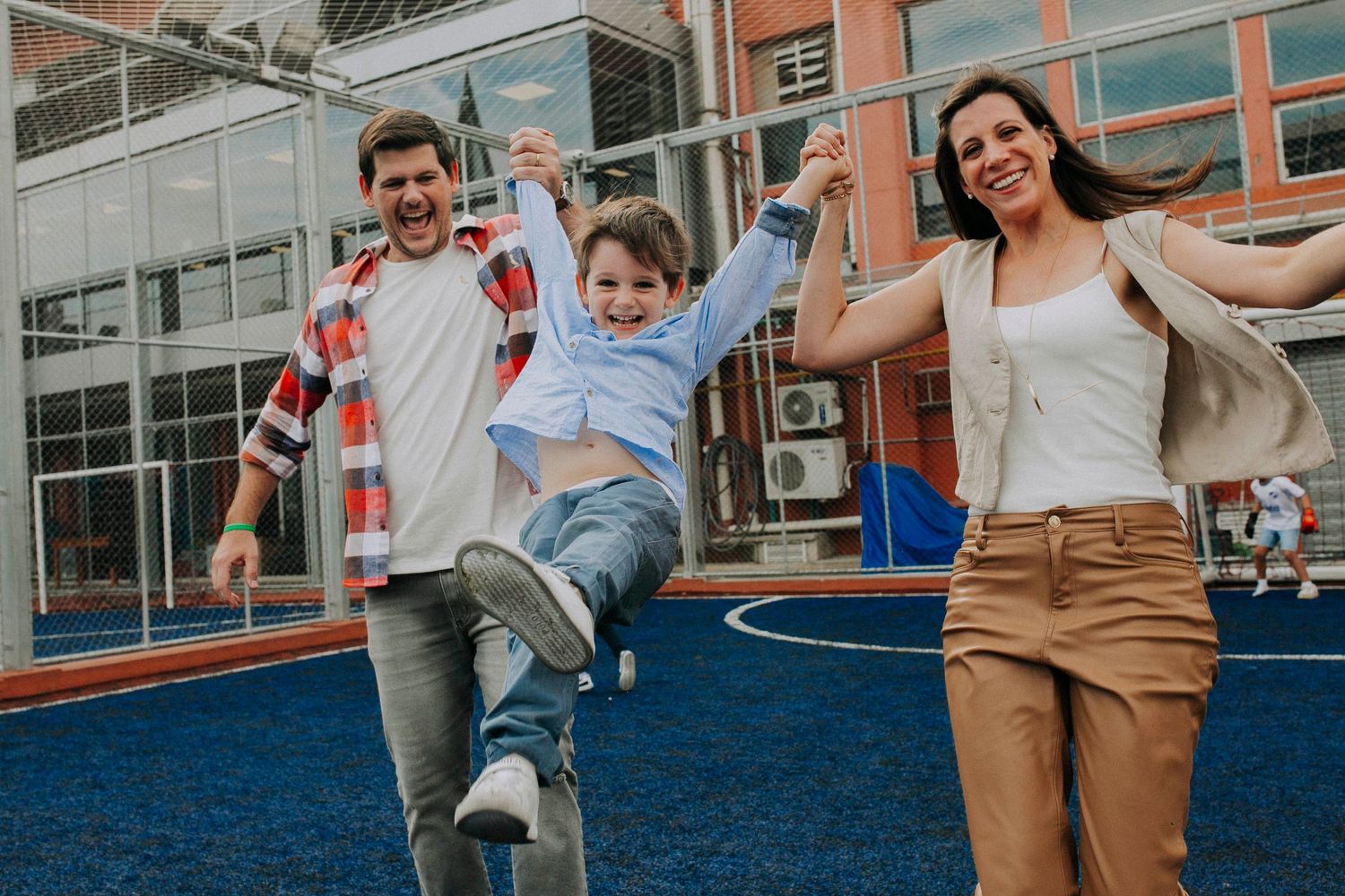 Three people enjoying a playful moment together on a blue outdoor surface by modern buildings.