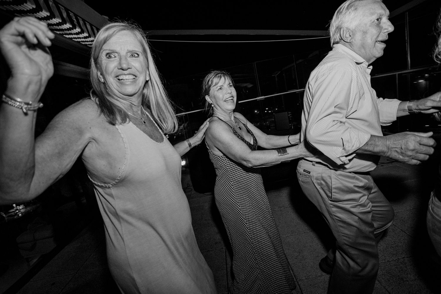 Black and white photo of three adults dancing joyfully at a party or wedding reception event.