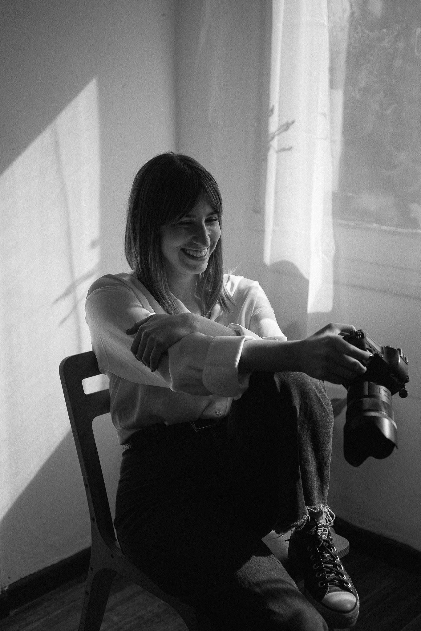 Black and white portrait of a photographer sitting with camera in natural window light.