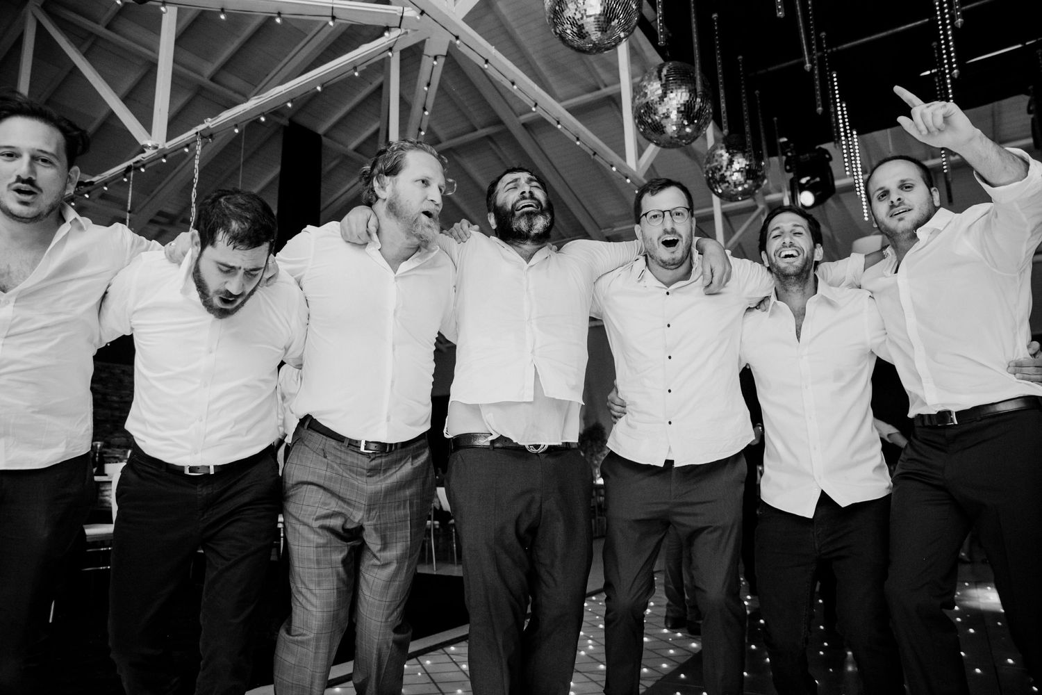 Group of friends in white shirts celebrating together at an indoor venue.