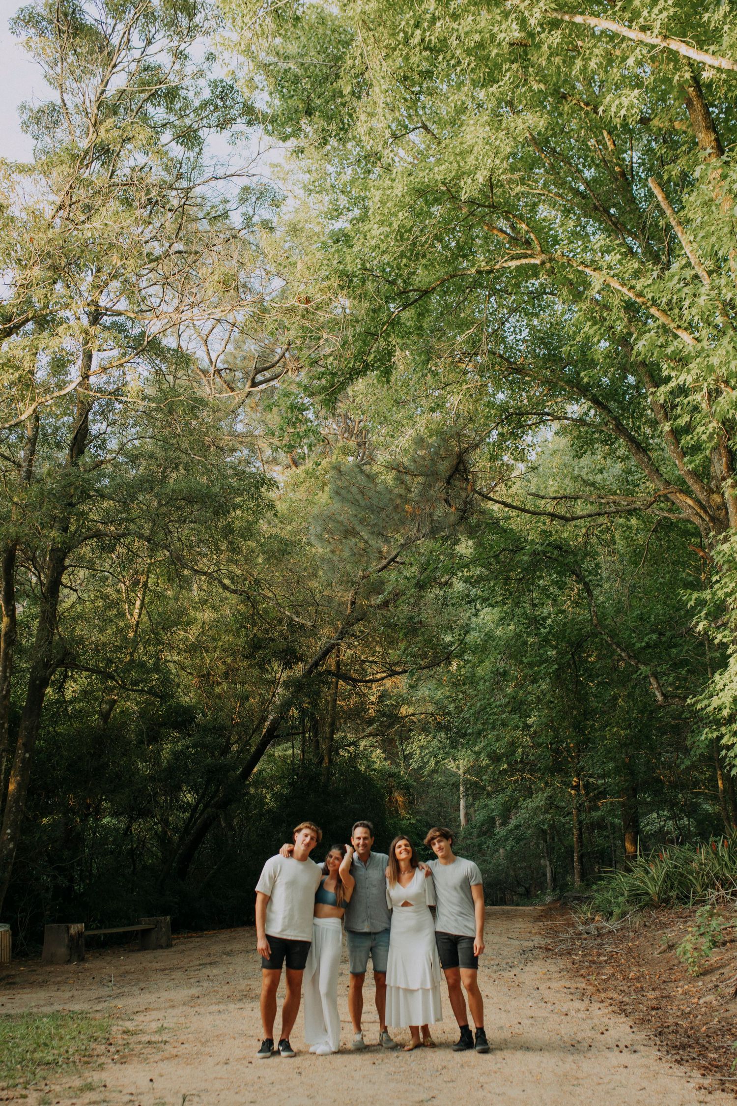 Group photo of friends standing together on a forest path surrounded by lush green trees.