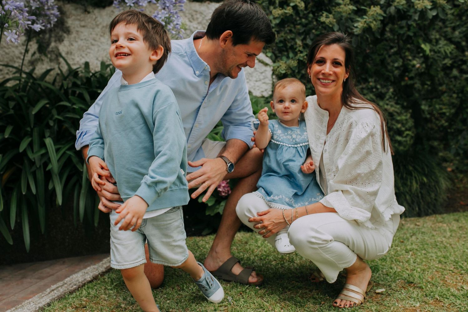 Family portrait in coordinated blue and white outfits against blooming garden backdrop.
