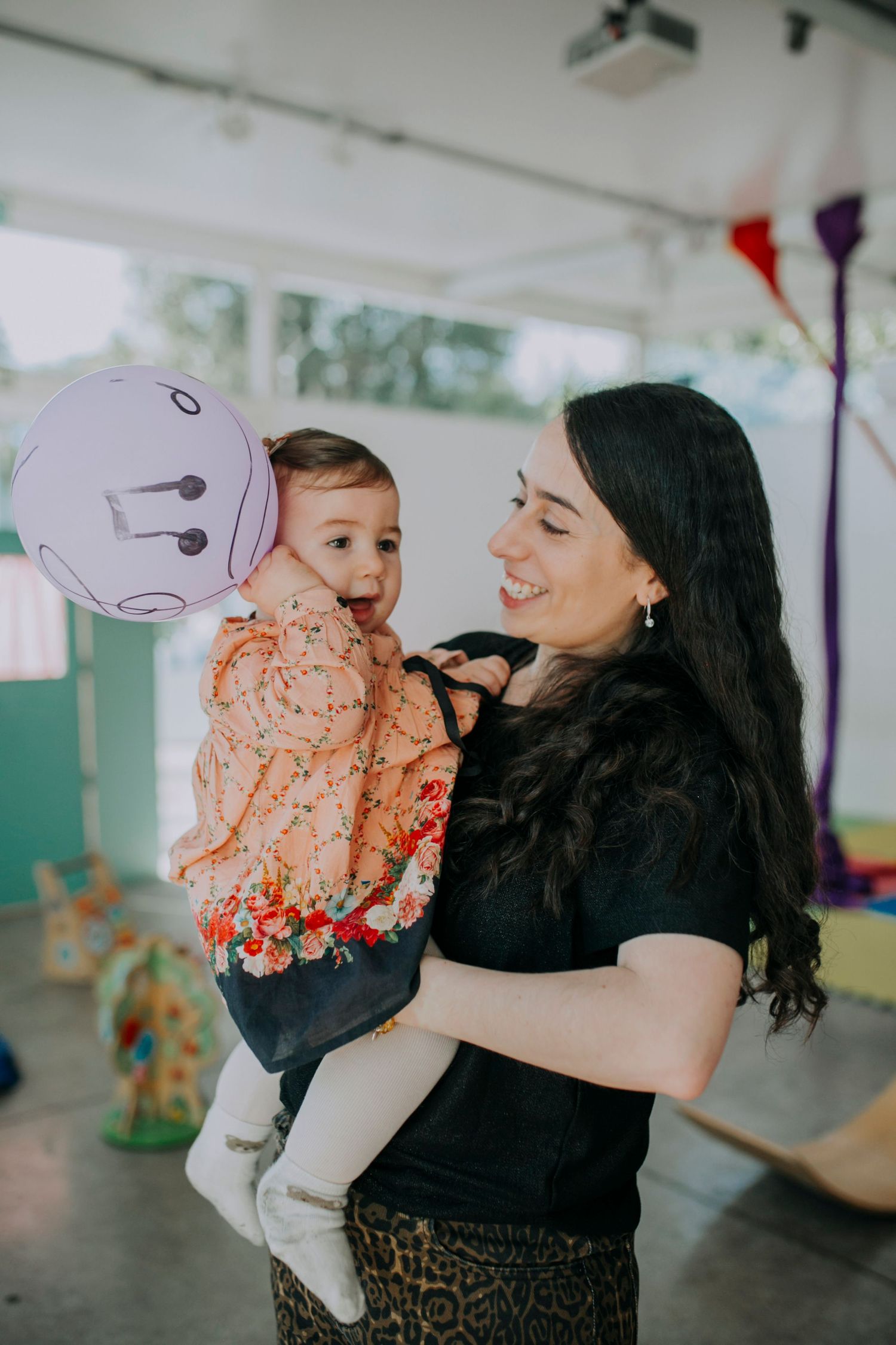 A joyful indoor celebration with balloons and decorations as mother holds excited child.