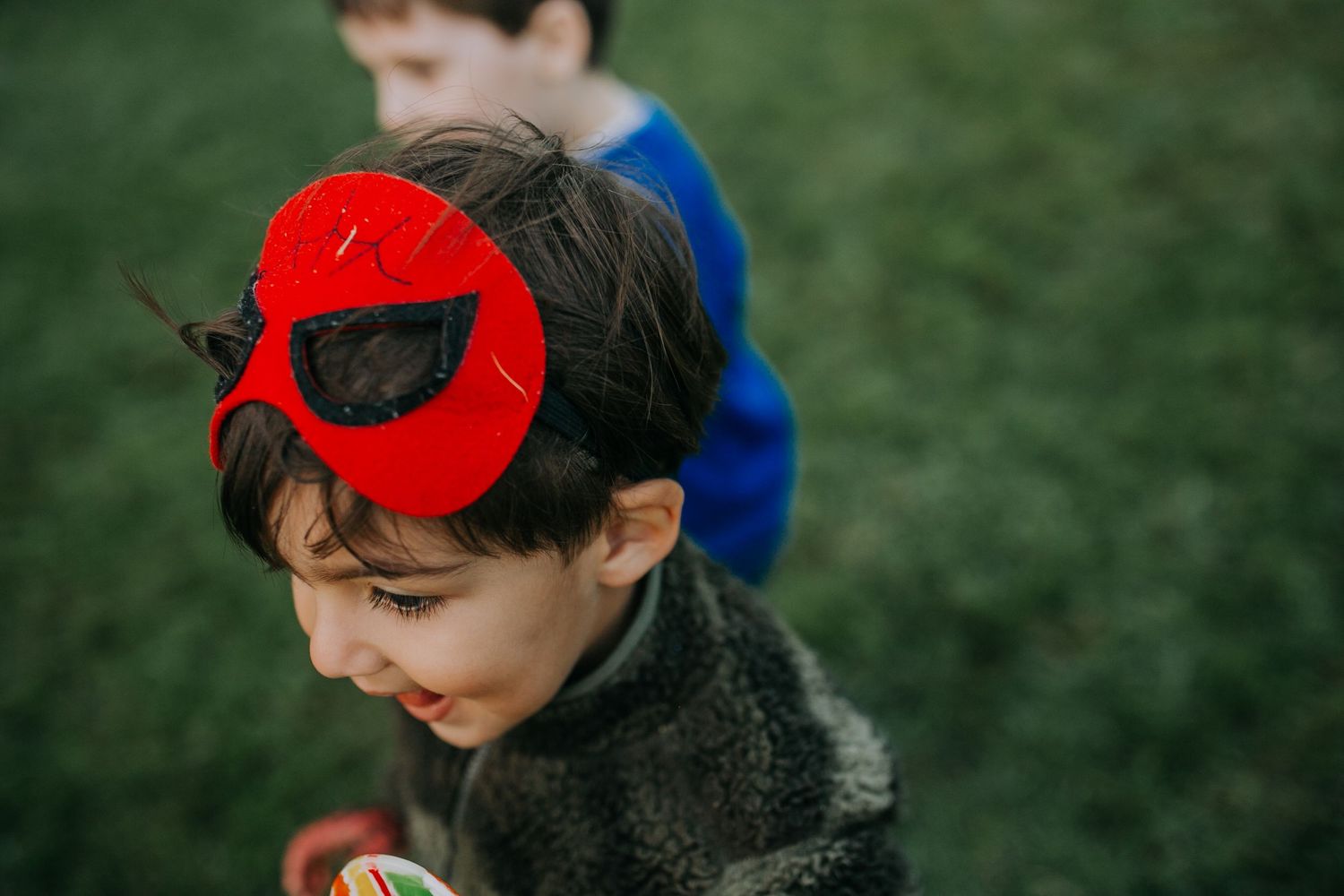 Child wearing a red superhero eye mask smiling while playing outside.