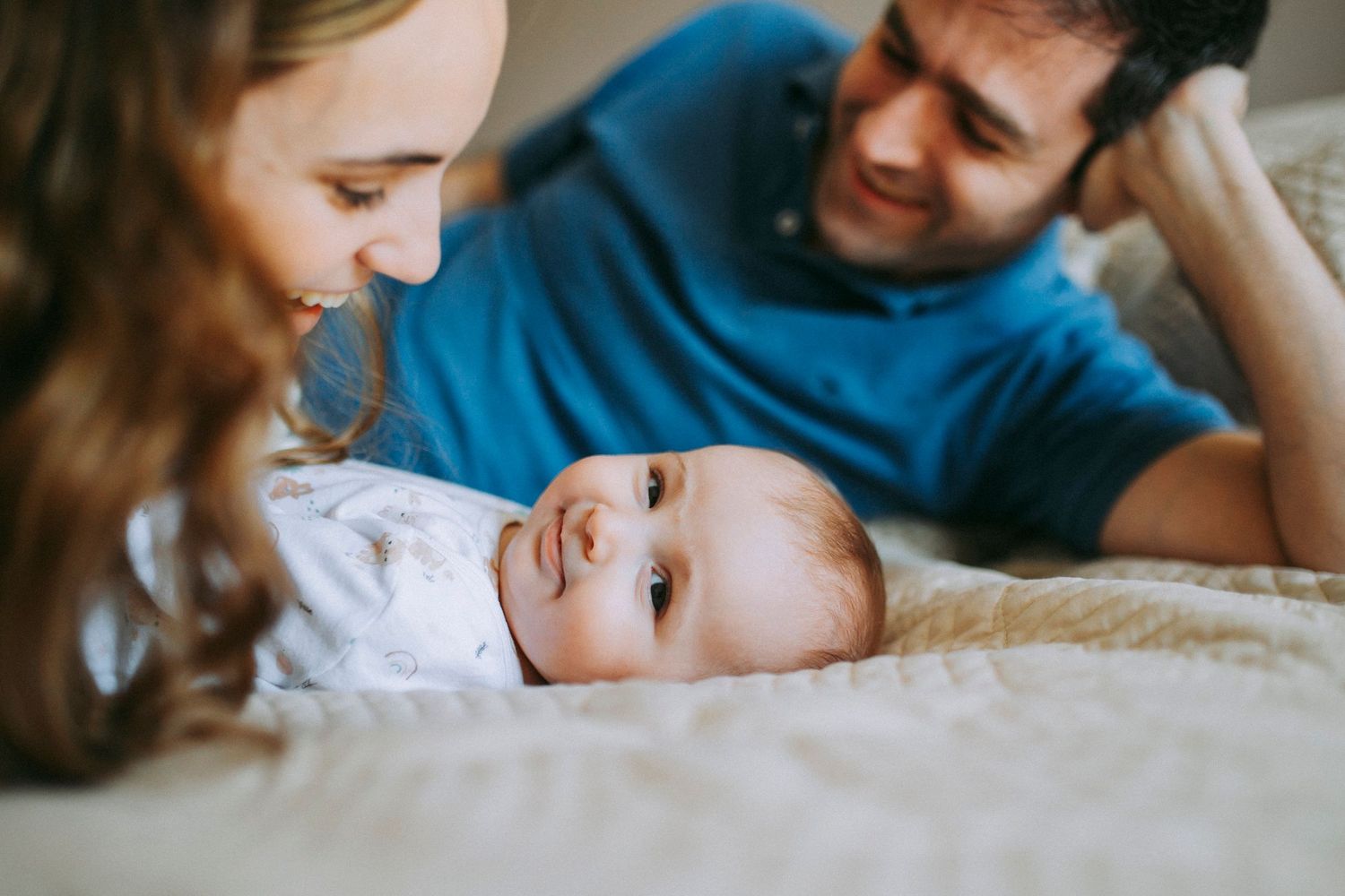 A peaceful moment between parents and their alert baby on a bed.
