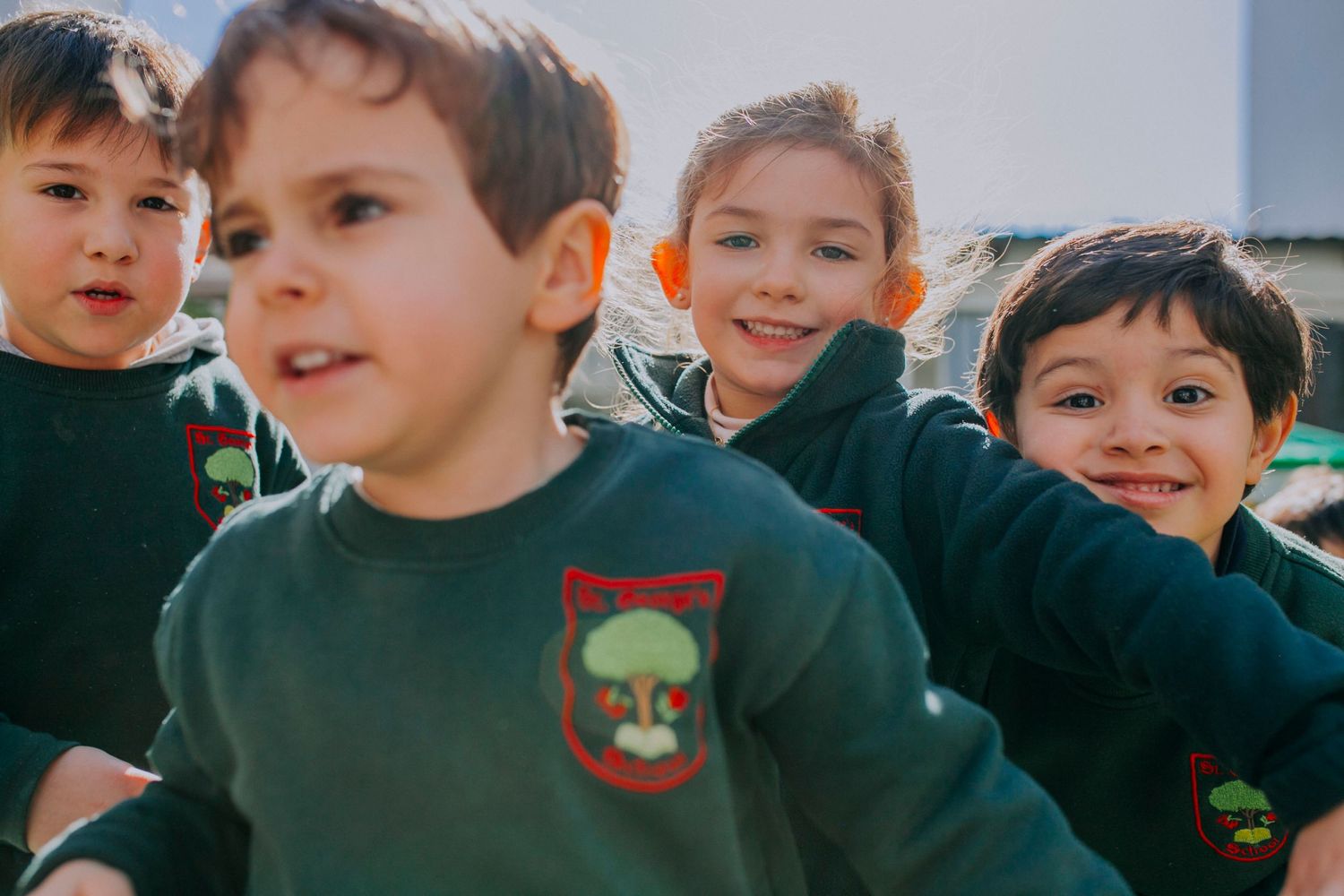 A group of young children in matching green school uniforms smiling together outdoors.
