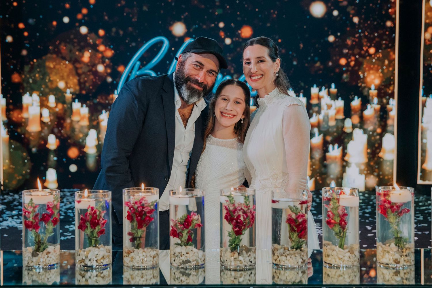 Family of three smiling at a festive celebration with elegant candle centerpieces and floral arrangements in glass vases.