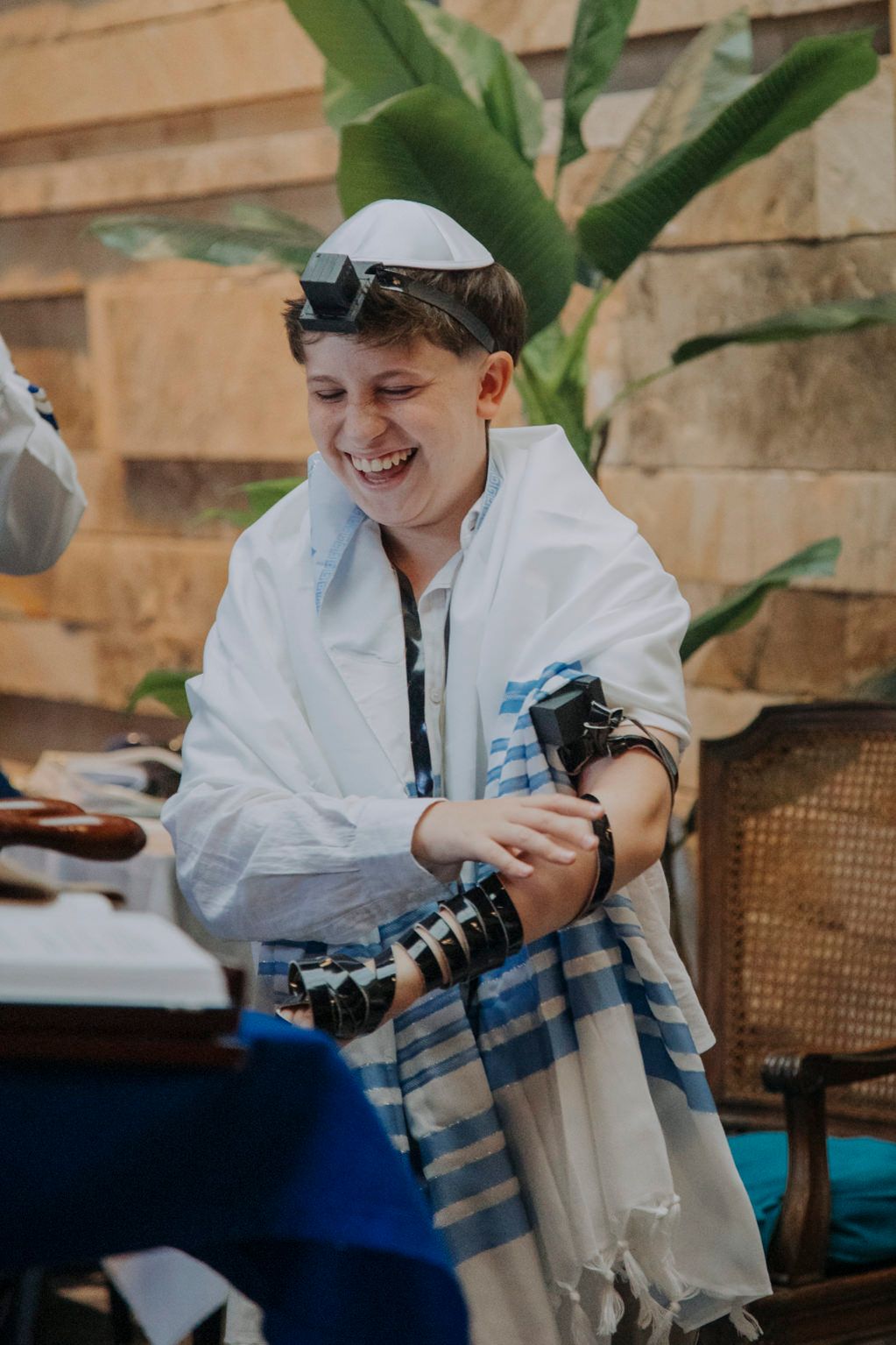 Smiling boy wearing tallit and tefillin during his Bar Mitzvah ceremony outdoors.