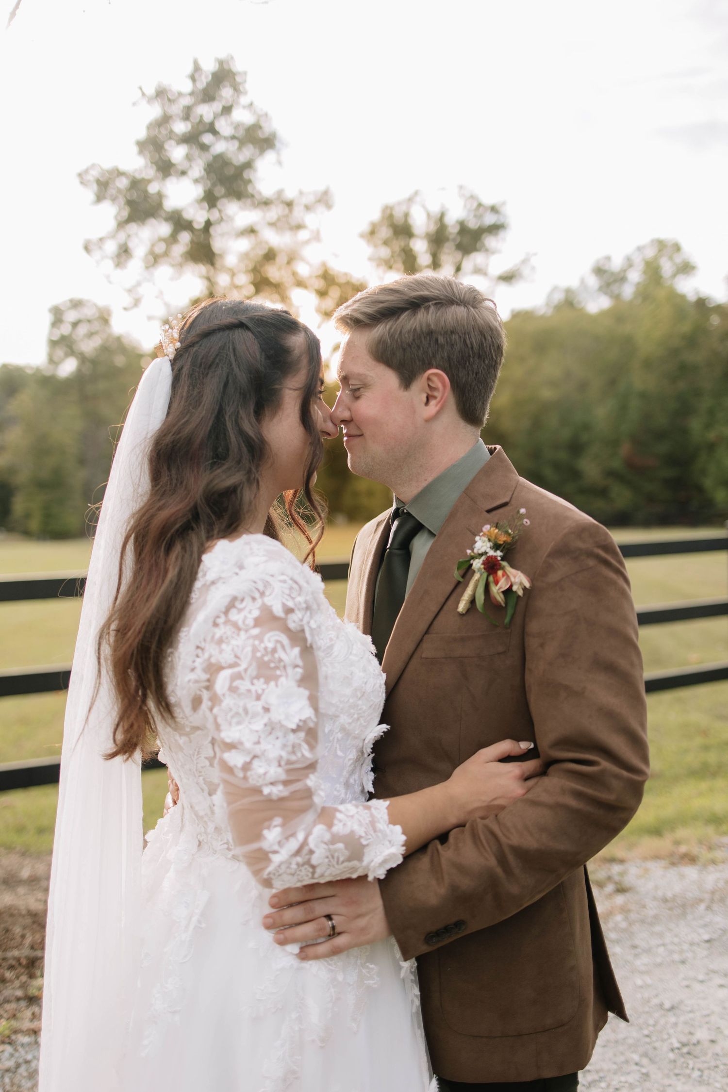 Romantic wedding moment captured on a gravel path with rustic brown fence in background.