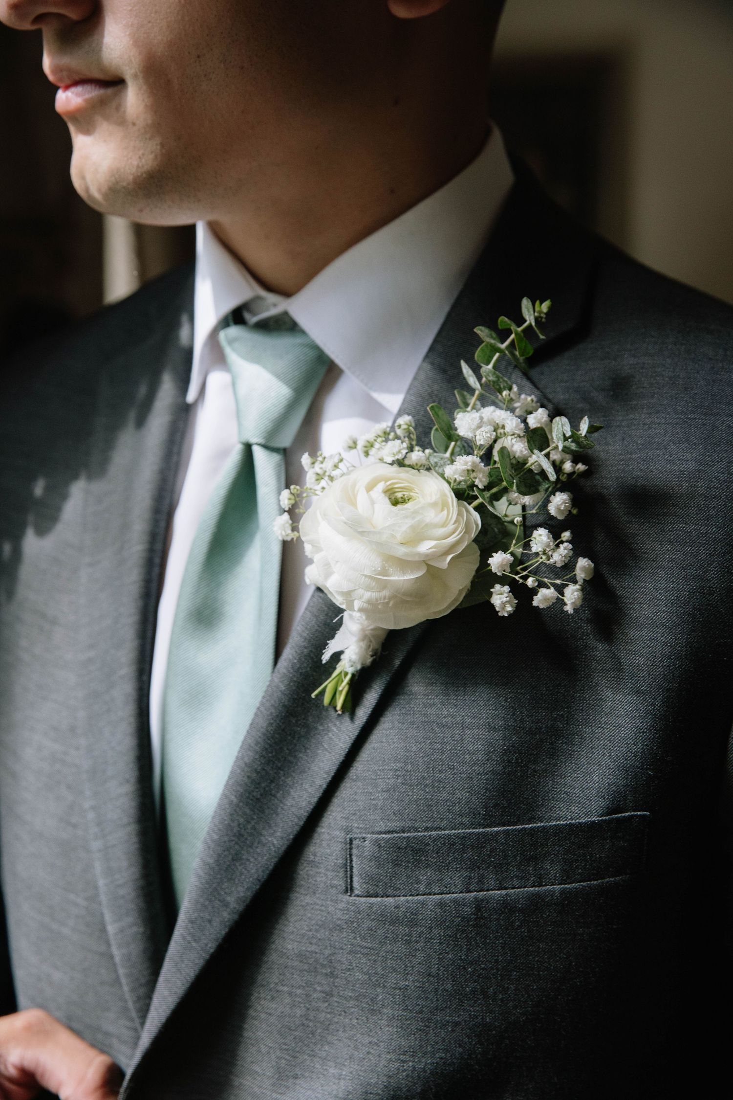 White floral boutonniere with baby's breath pinned to a grey suit jacket.