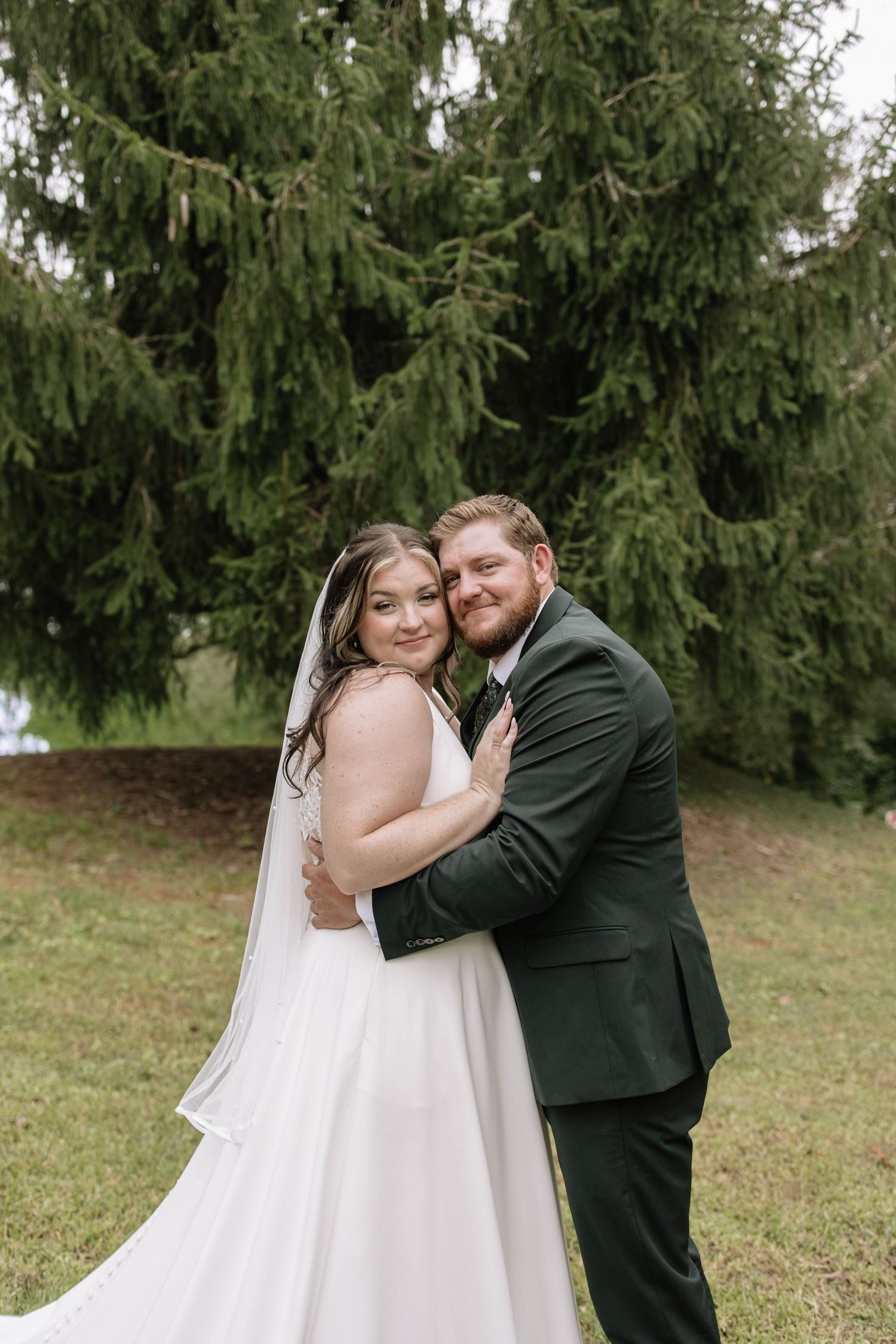 Wedding couple sharing intimate moments against evergreen trees in outdoor setting.