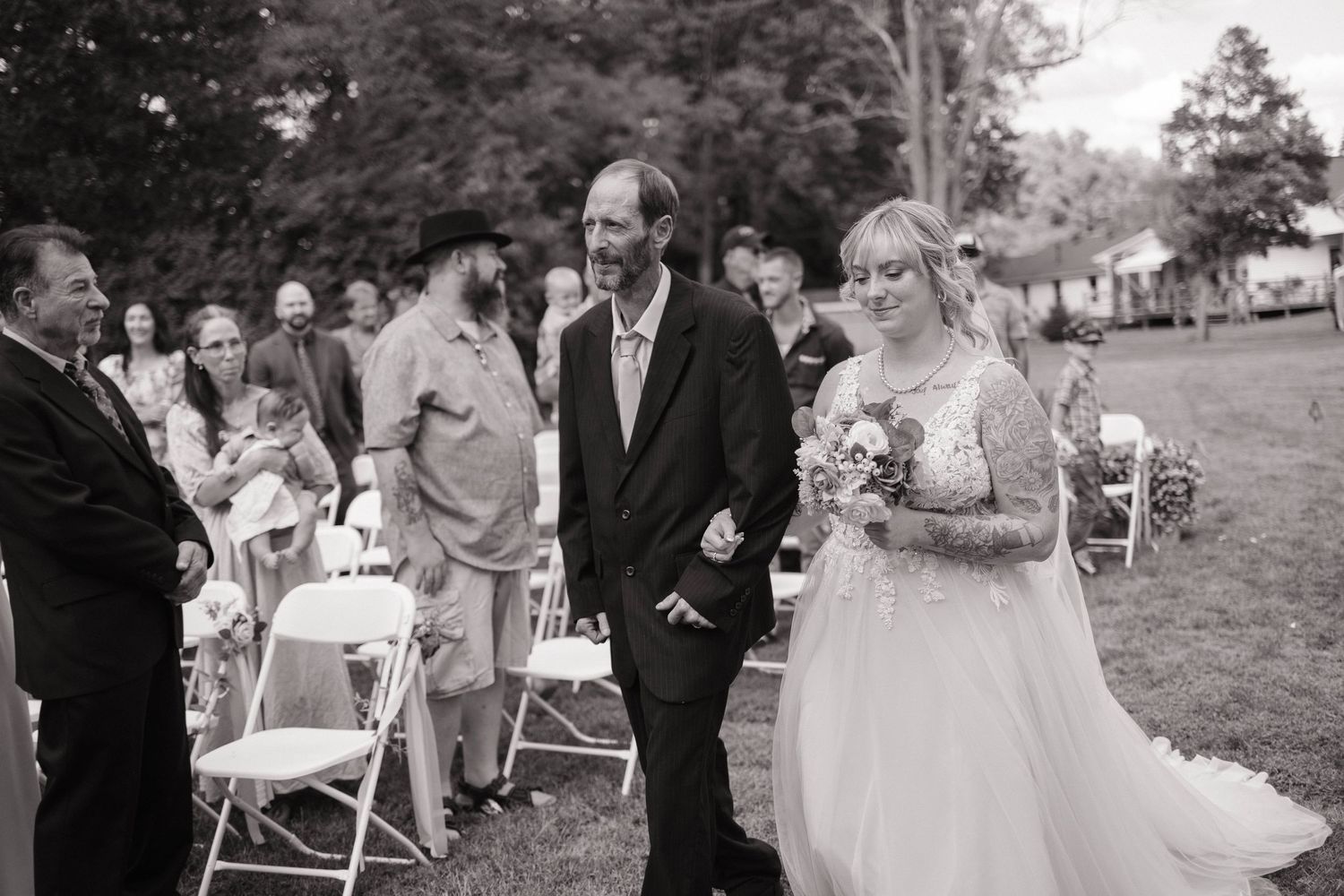 Wedding ceremony guests seated in white chairs on a lawn during an outdoor celebration.