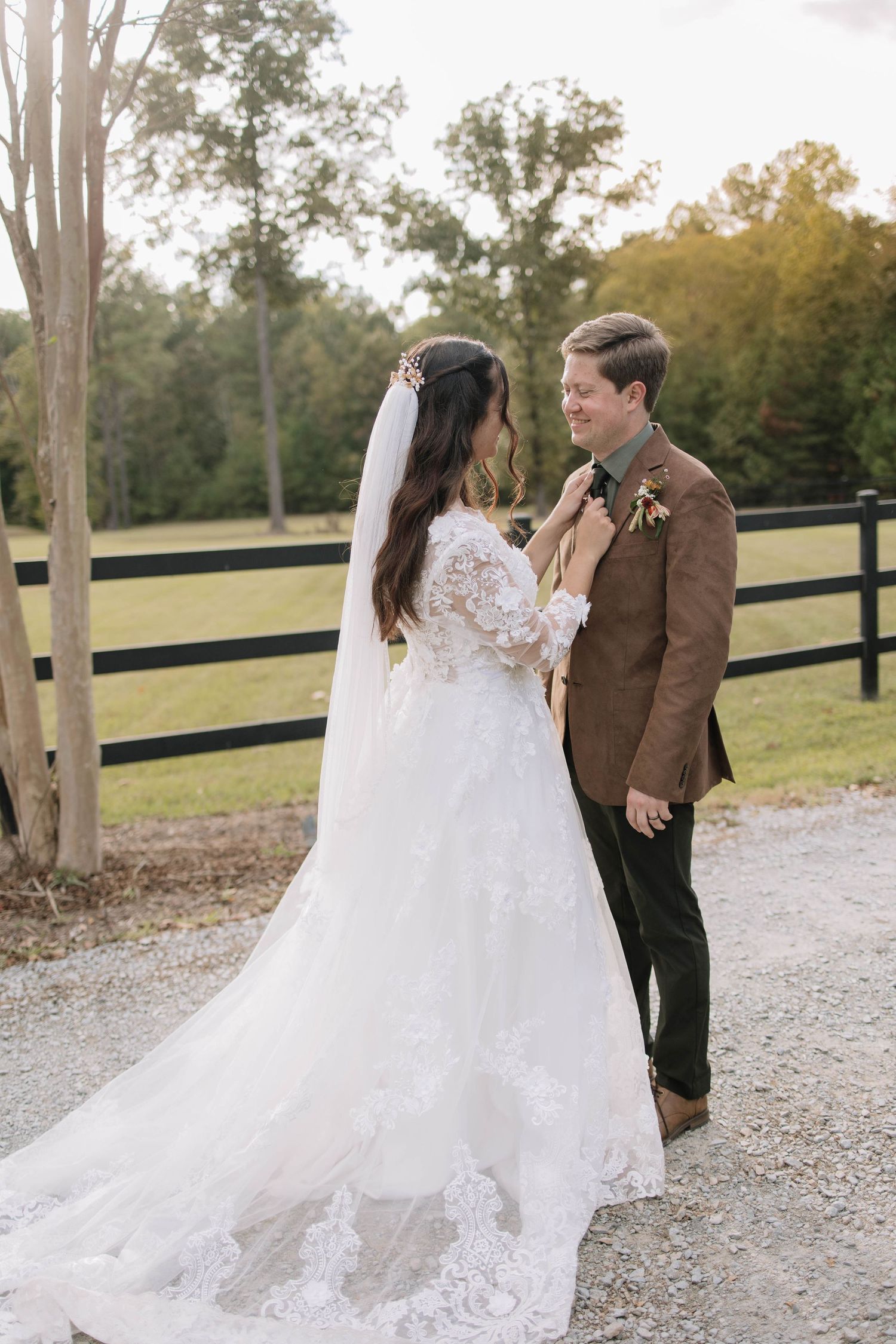 Wedding couple poses on gravel path with flowing white dress and autumn trees in background.