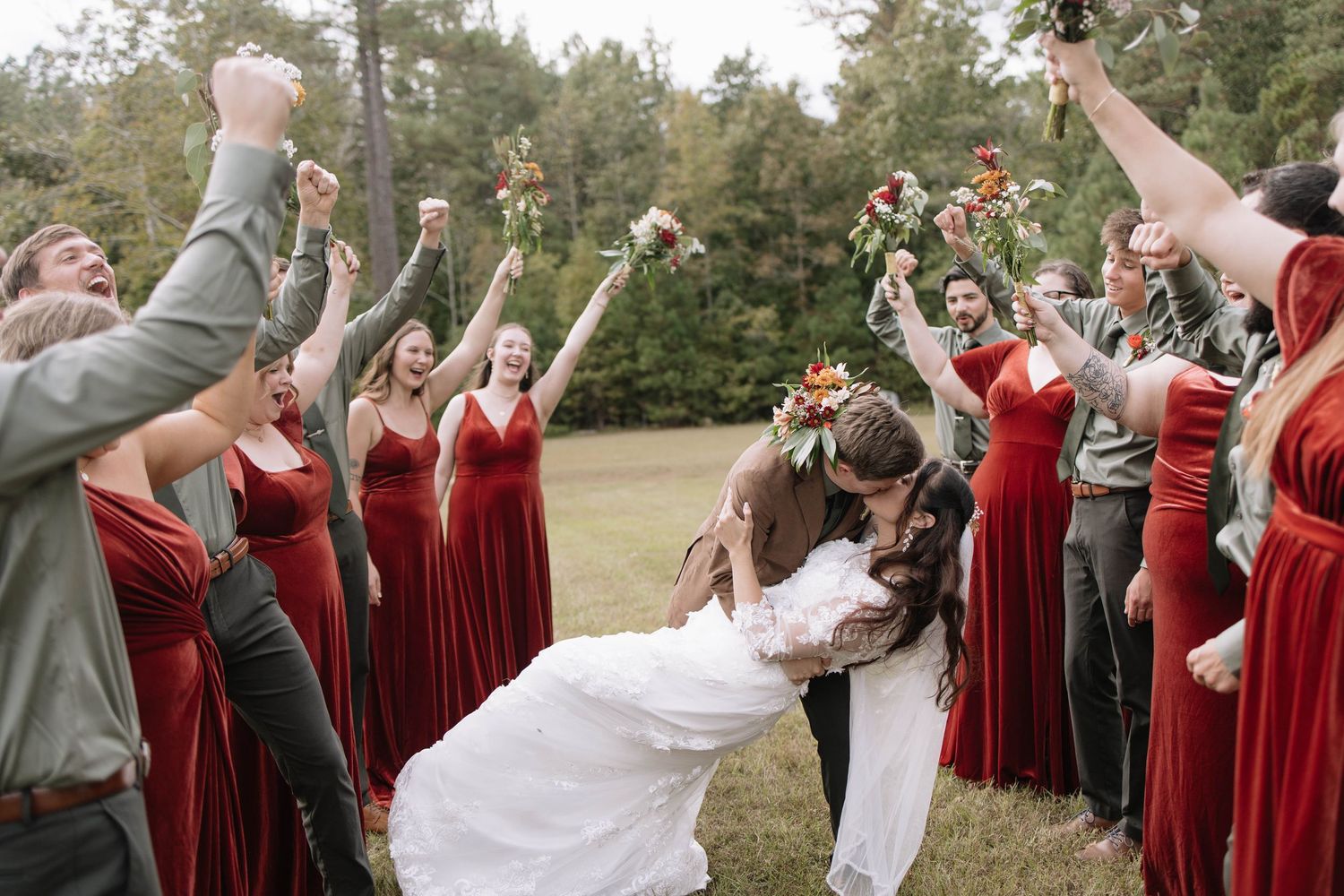 Wedding party celebrates with energetic poses in outdoor setting.