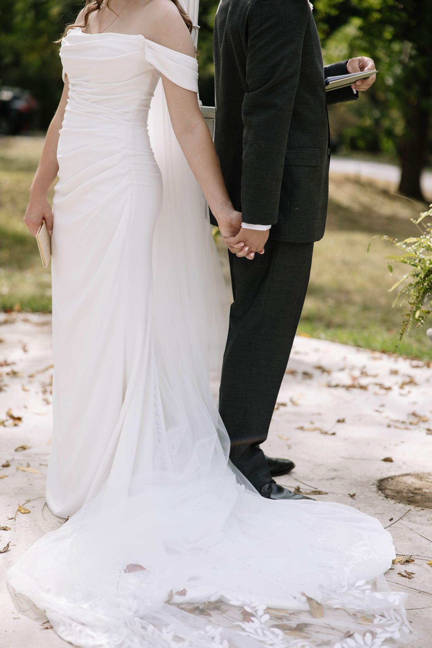 Detail shot of wedding dress train and couple's feet on ground covered with fallen leaves.