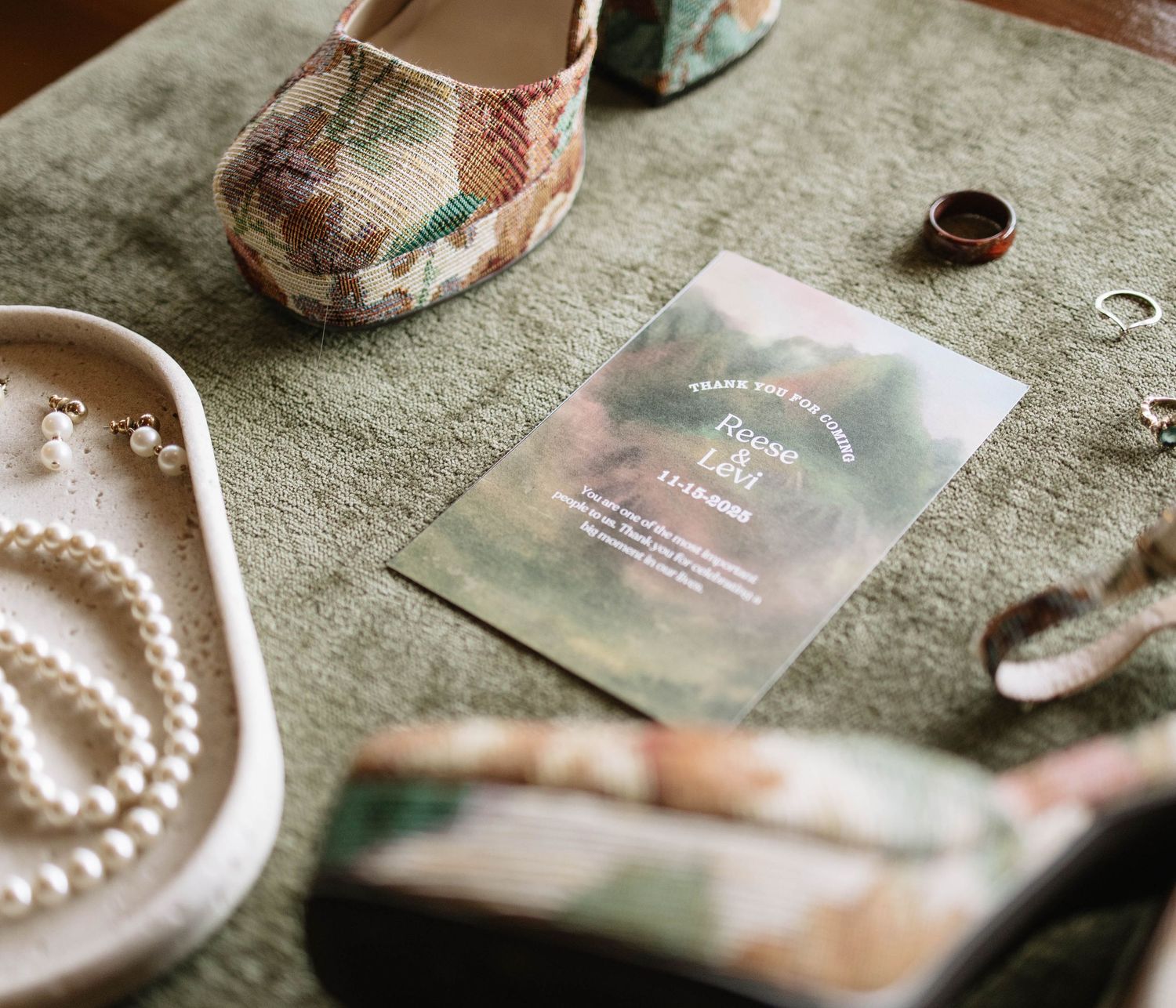 Wedding detail shot featuring pearl jewelry and invitation cards on textured surface.