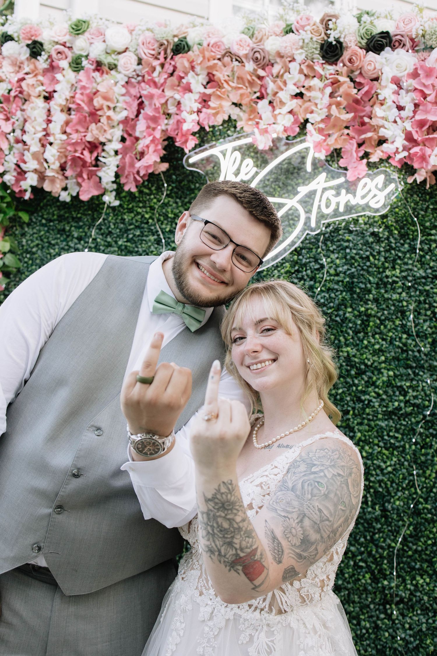 Playful wedding photo against floral wall backdrop with pink blooms.