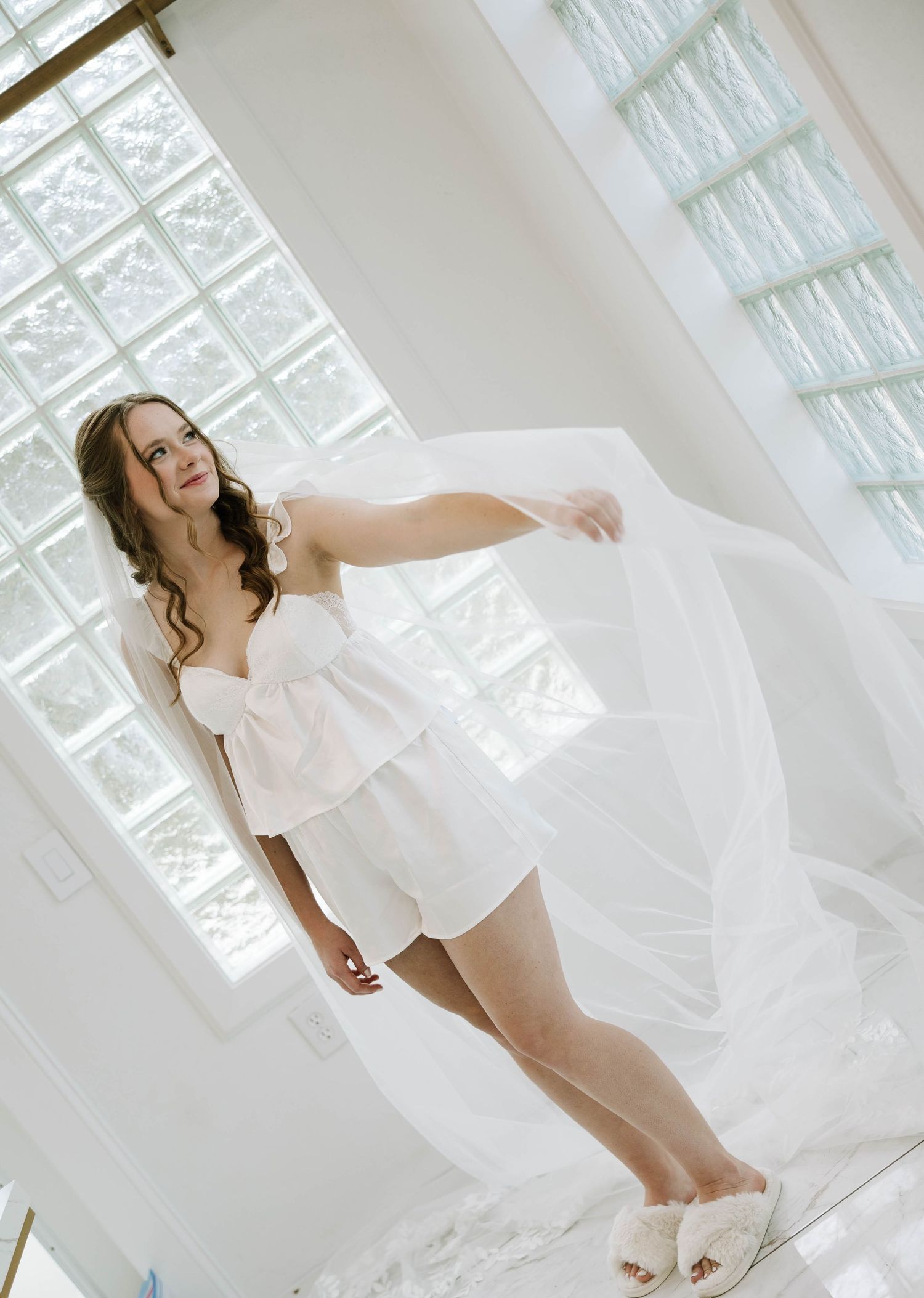 Ethereal bridal portrait in white room with flowing dress and natural light.
