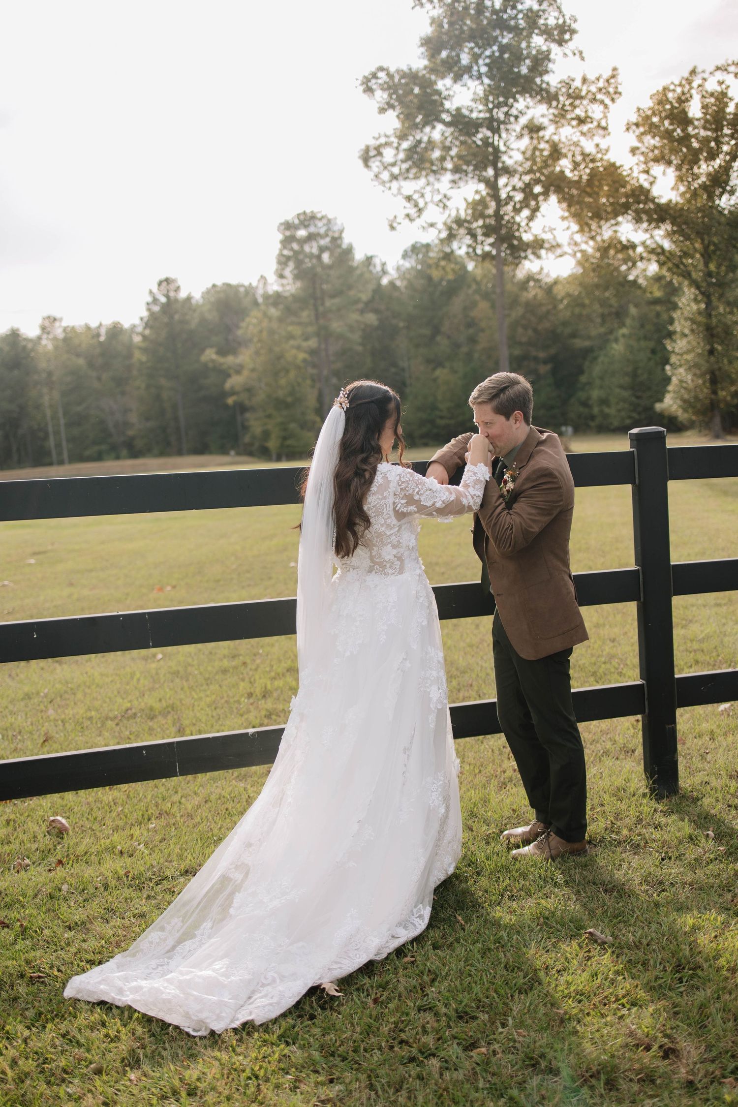 Romantic wedding couple poses in a field at sunset with a black fence in the background.