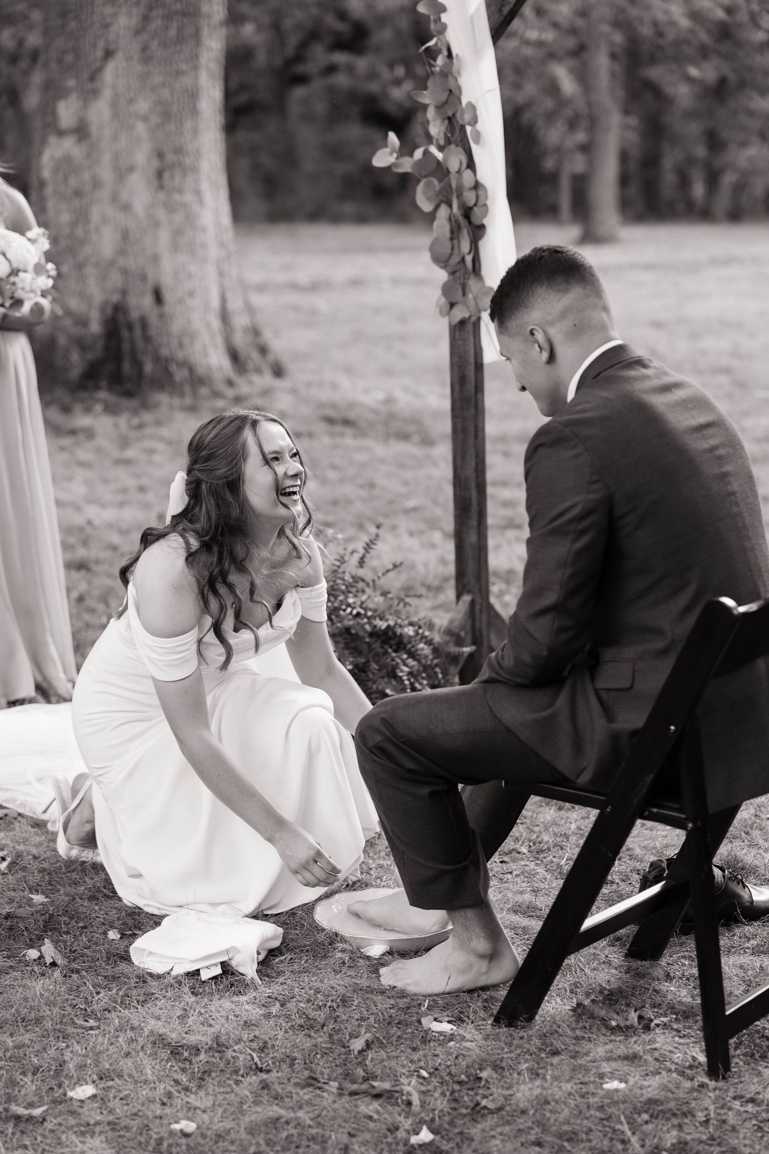Black and white photo of a couple playfully sitting on a swing together at their wedding.