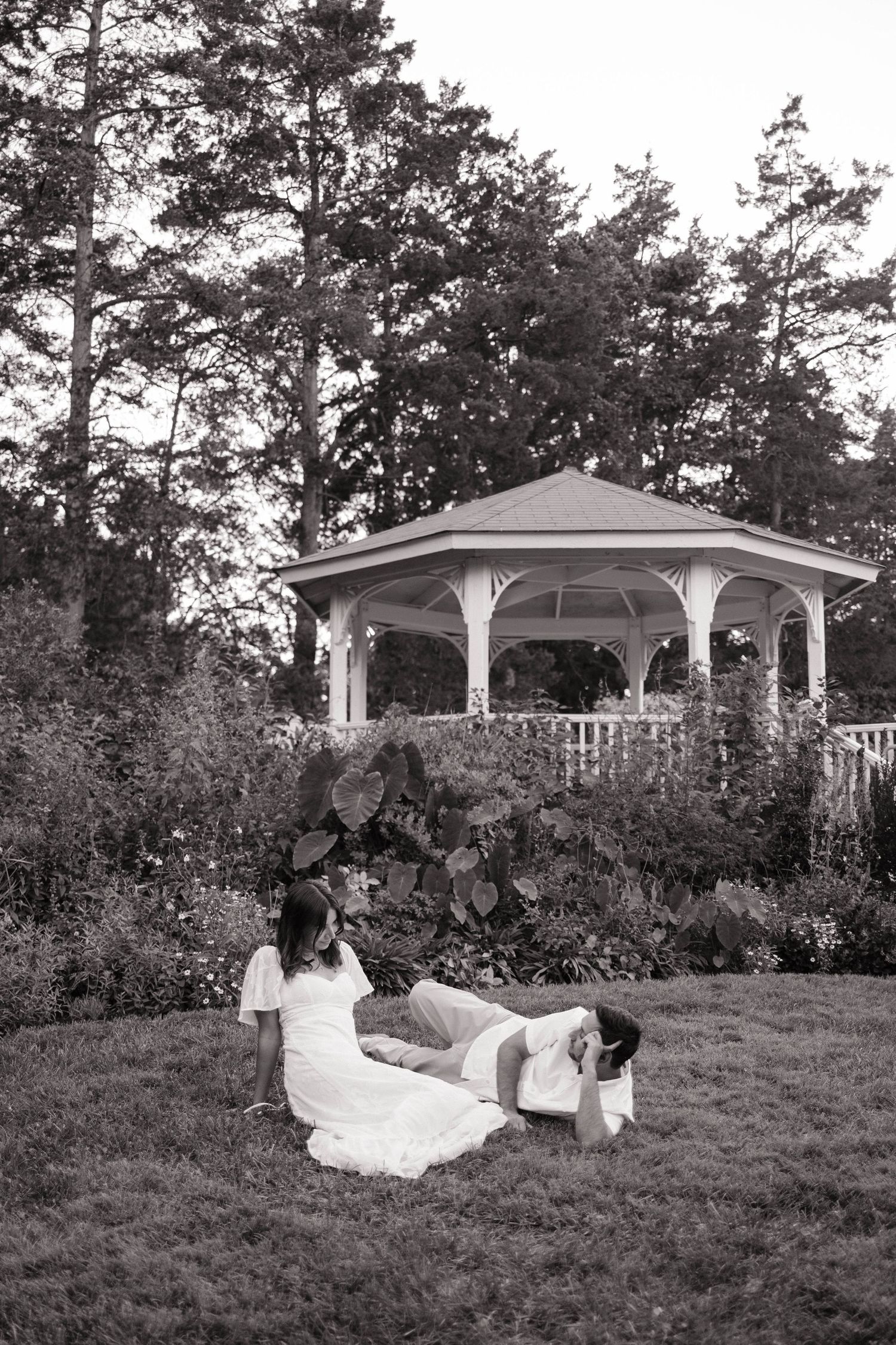 Black and white portrait of couple near gazebo in garden setting.