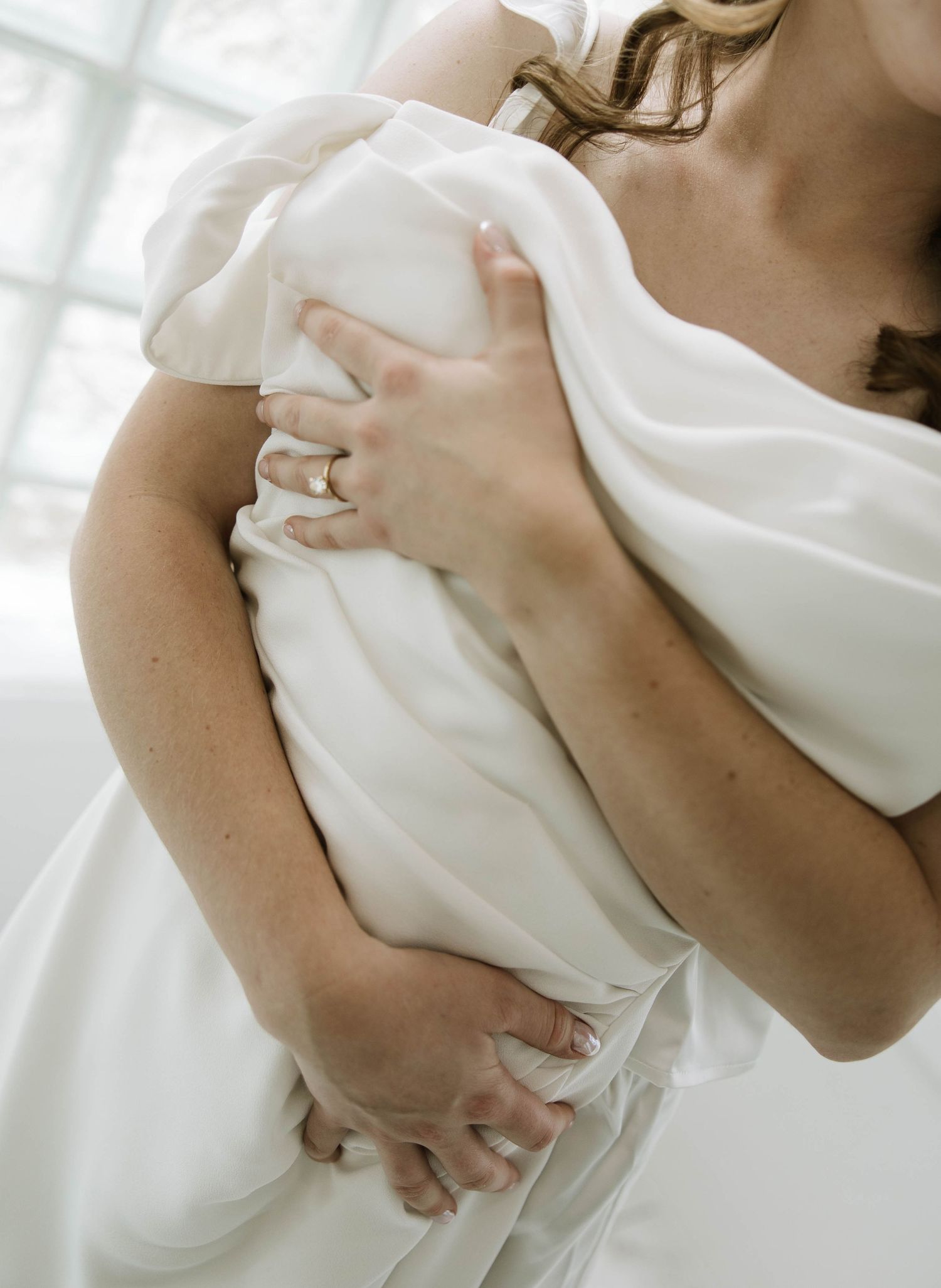 Close-up details of someone holding white fabric against themselves in a sunlit room.