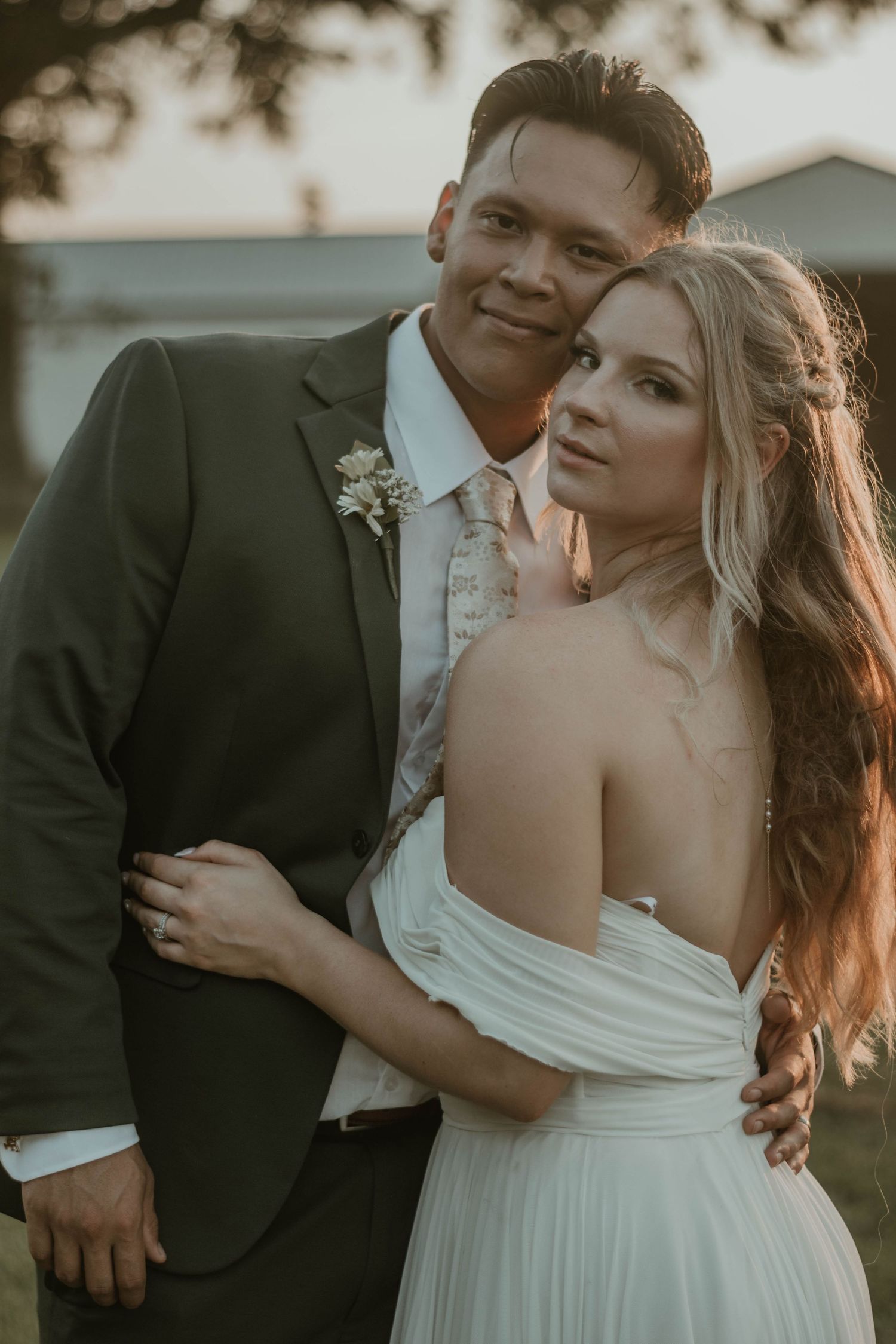 A romantic sunset moment captured between newlyweds in formal wedding attire embracing outdoors.