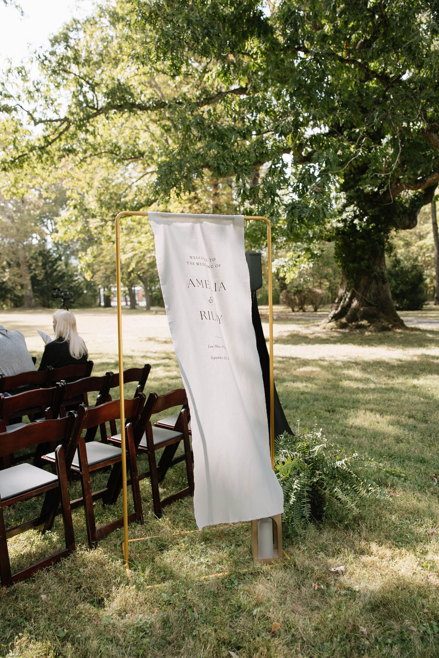 White signs on wooden stakes line up along a grassy outdoor wedding ceremony venue.