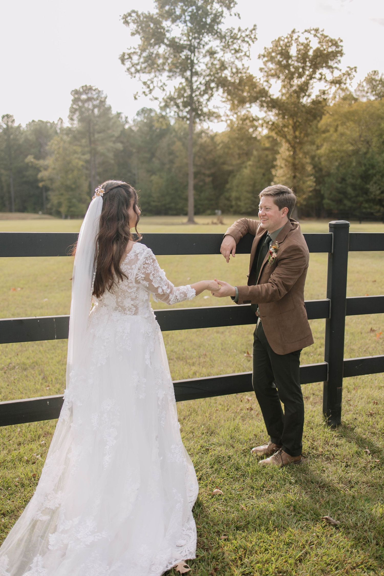 Playful wedding couple interacts by wooden fence during outdoor photo session.