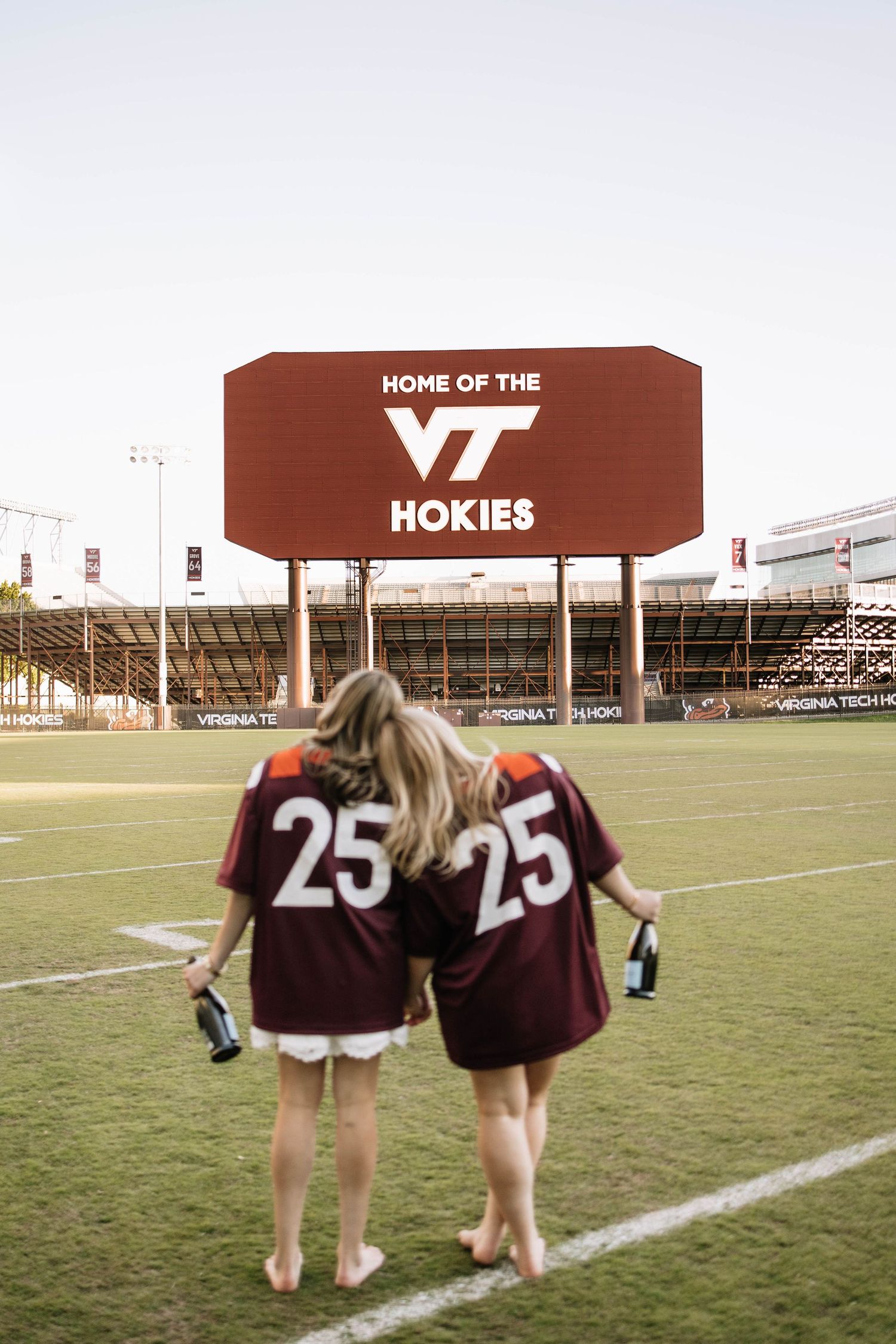 Two girls in matching Virginia Tech Hokies #25 jerseys stand on the field at Lane Stadium.