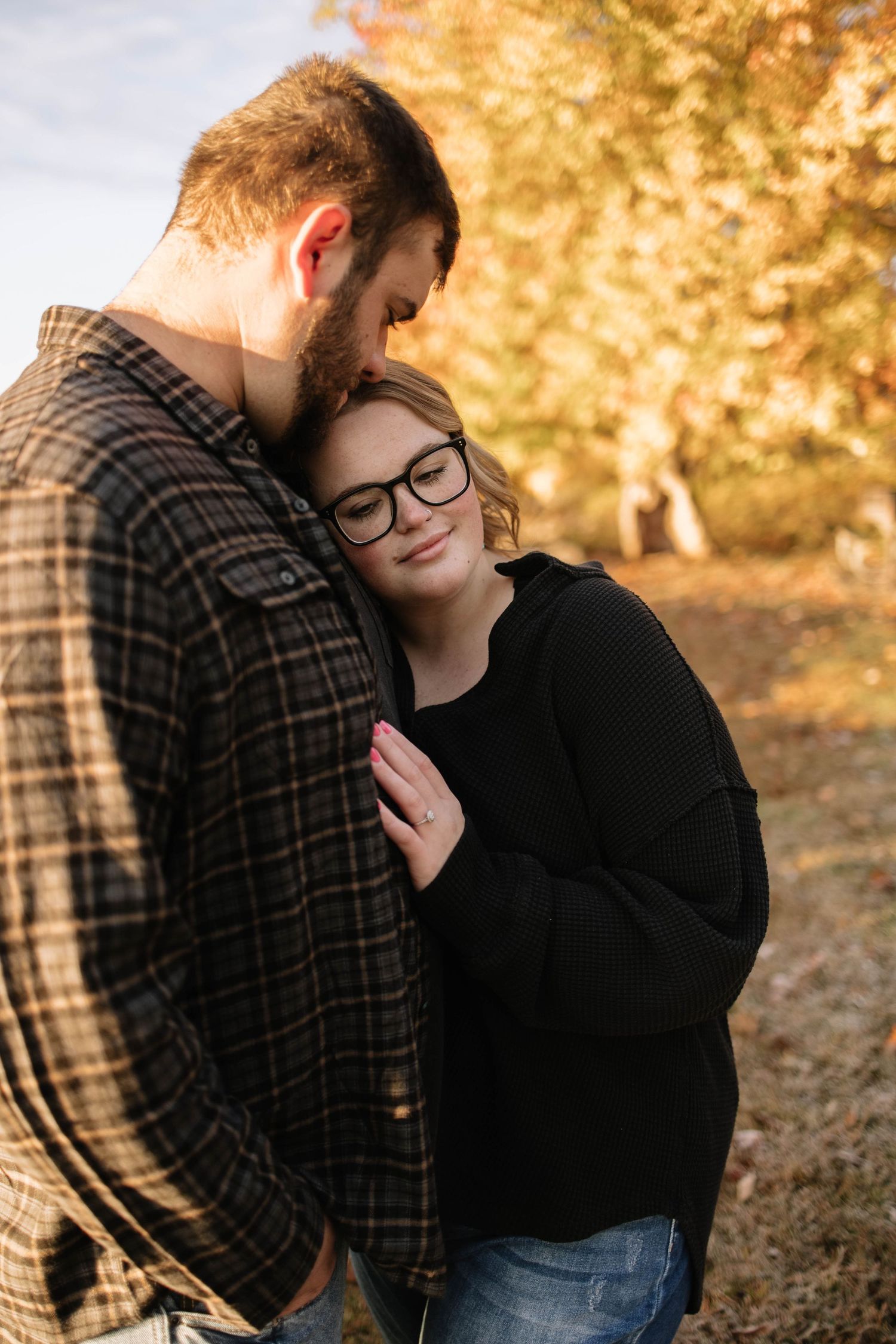 A romantic autumn photoshoot showing a couple embracing under golden fall foliage.