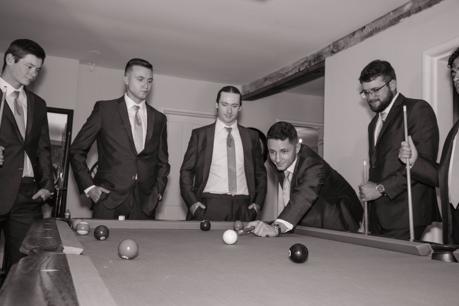 Black and white photo of groomsmen playing pool at a wedding reception.