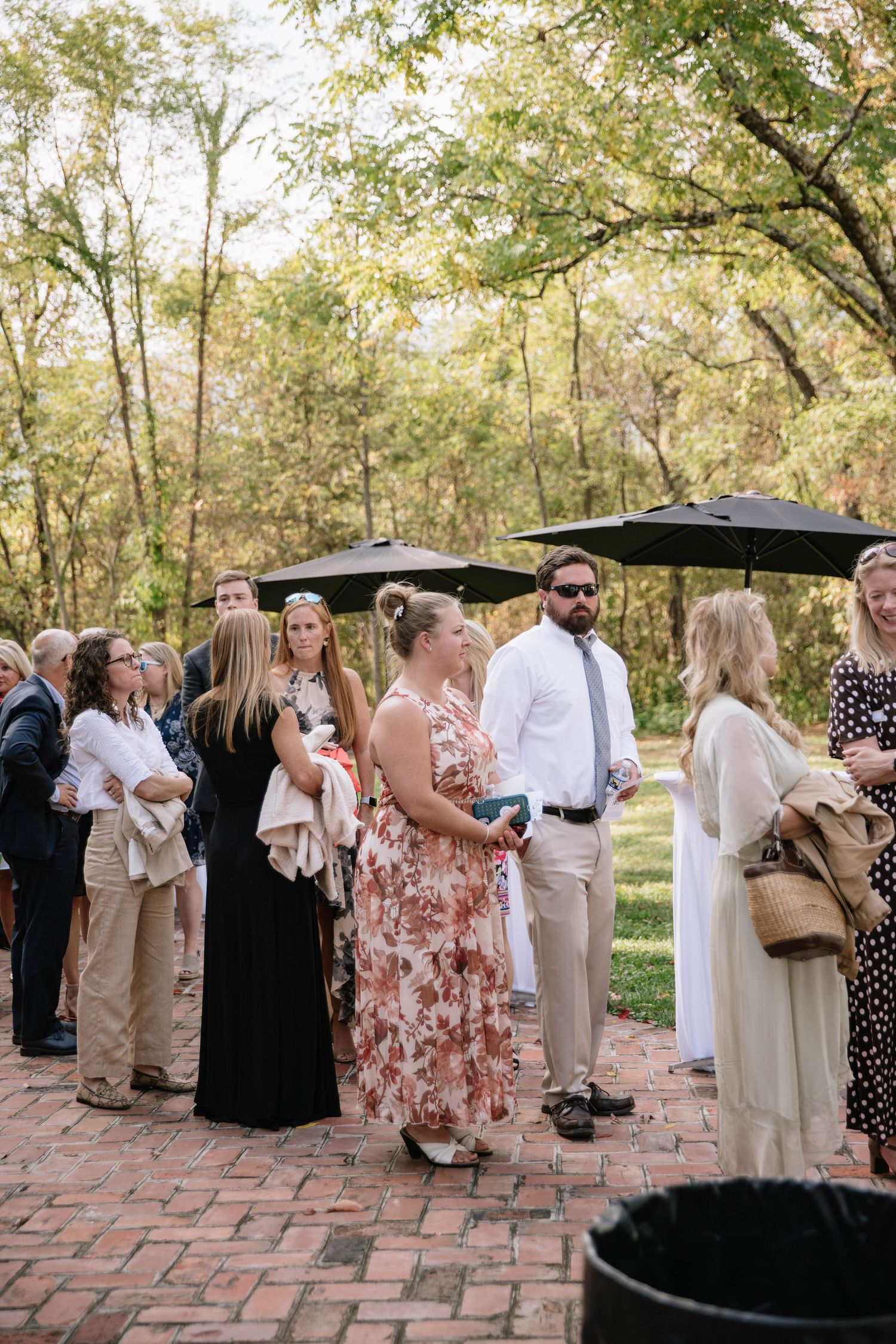 Wedding guests mingling on a brick patio surrounded by lush greenery.