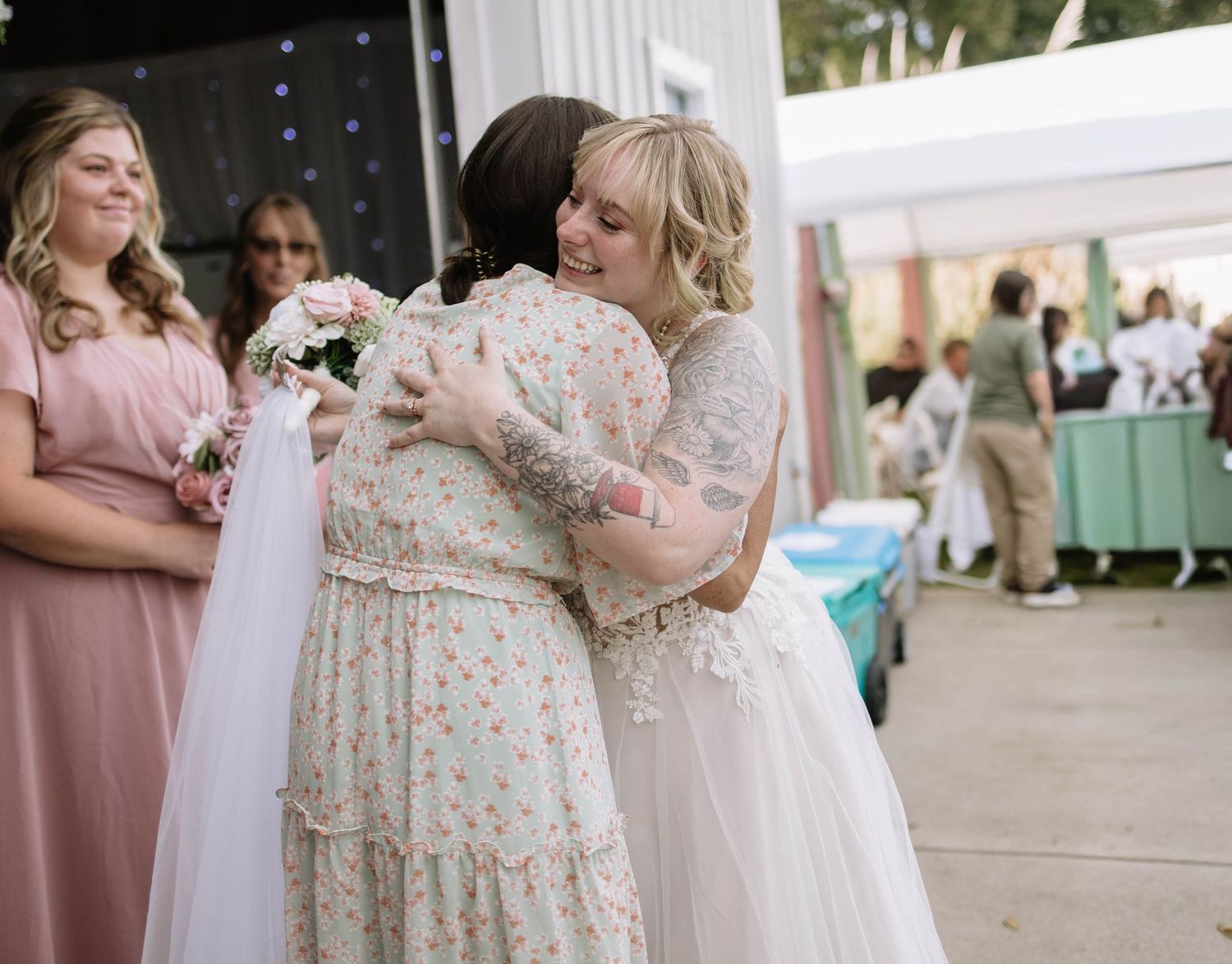 Wedding reception scene with bridesmaids in pink dresses under a white tent.