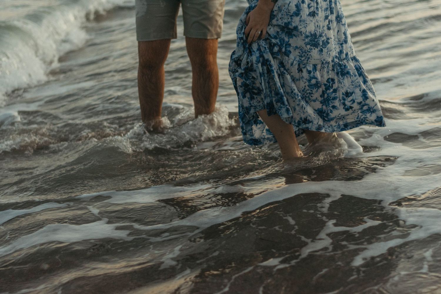 Couple splashing in water at beach during sunset photoshoot.