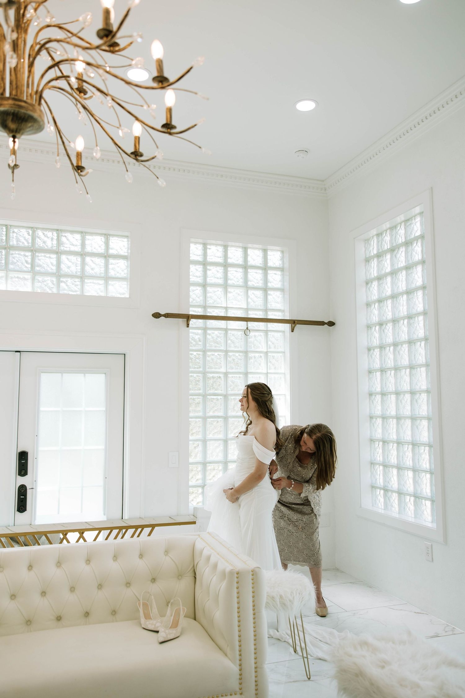 Getting ready moments in an elegant white room with chandelier and tufted furniture.