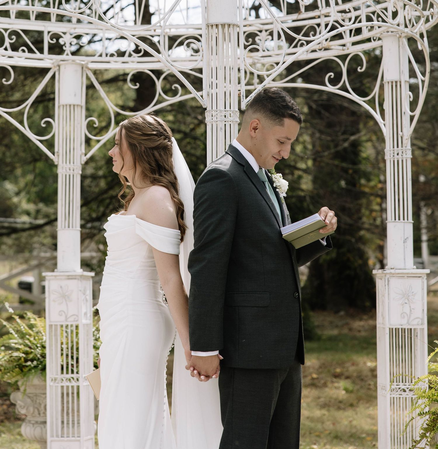 Wedding couple shares intimate first look moments under an ornate white gazebo surrounded by fall foliage.