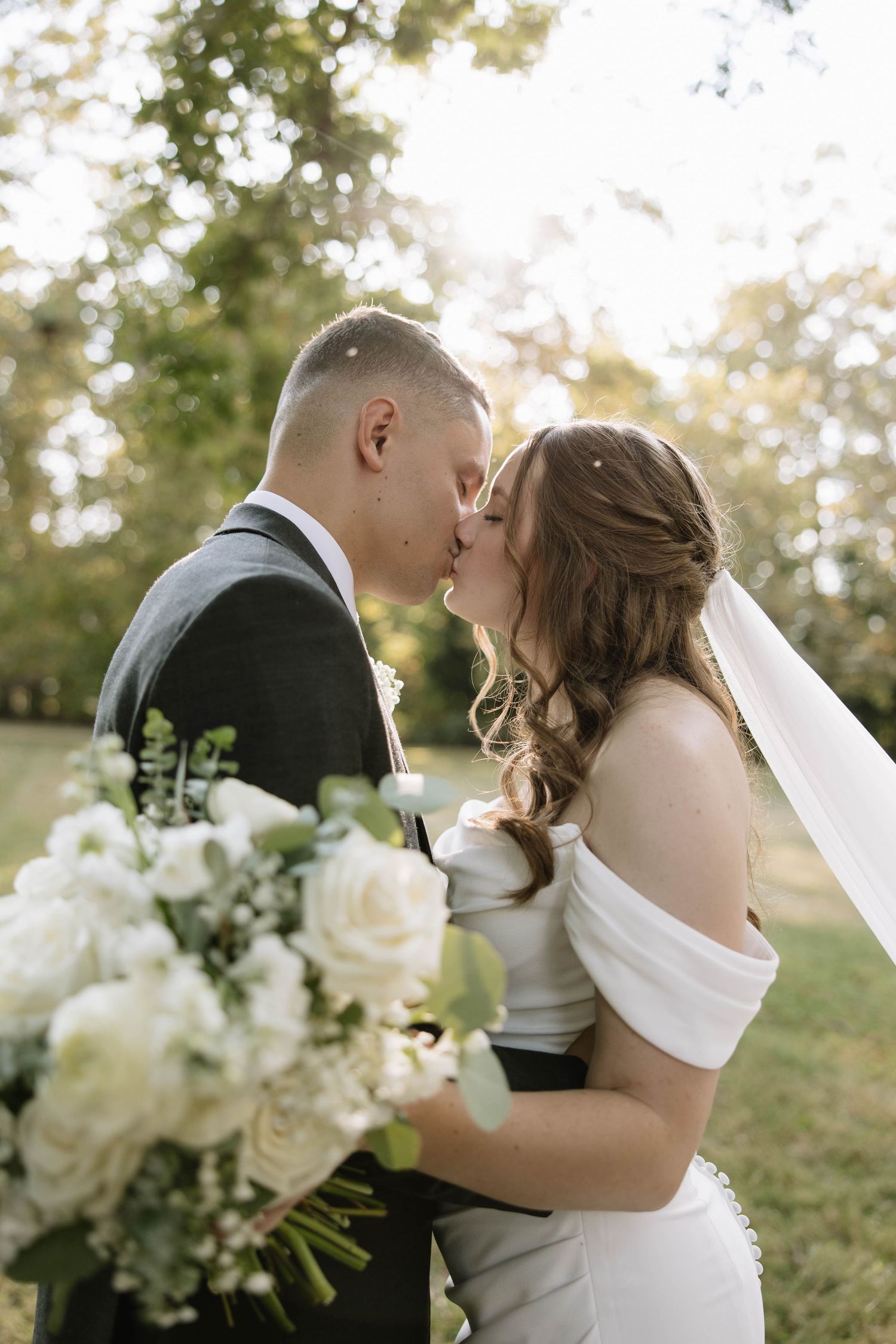 Romantic wedding couple shares intimate kisses in a series of outdoor portraits with white floral bouquet.