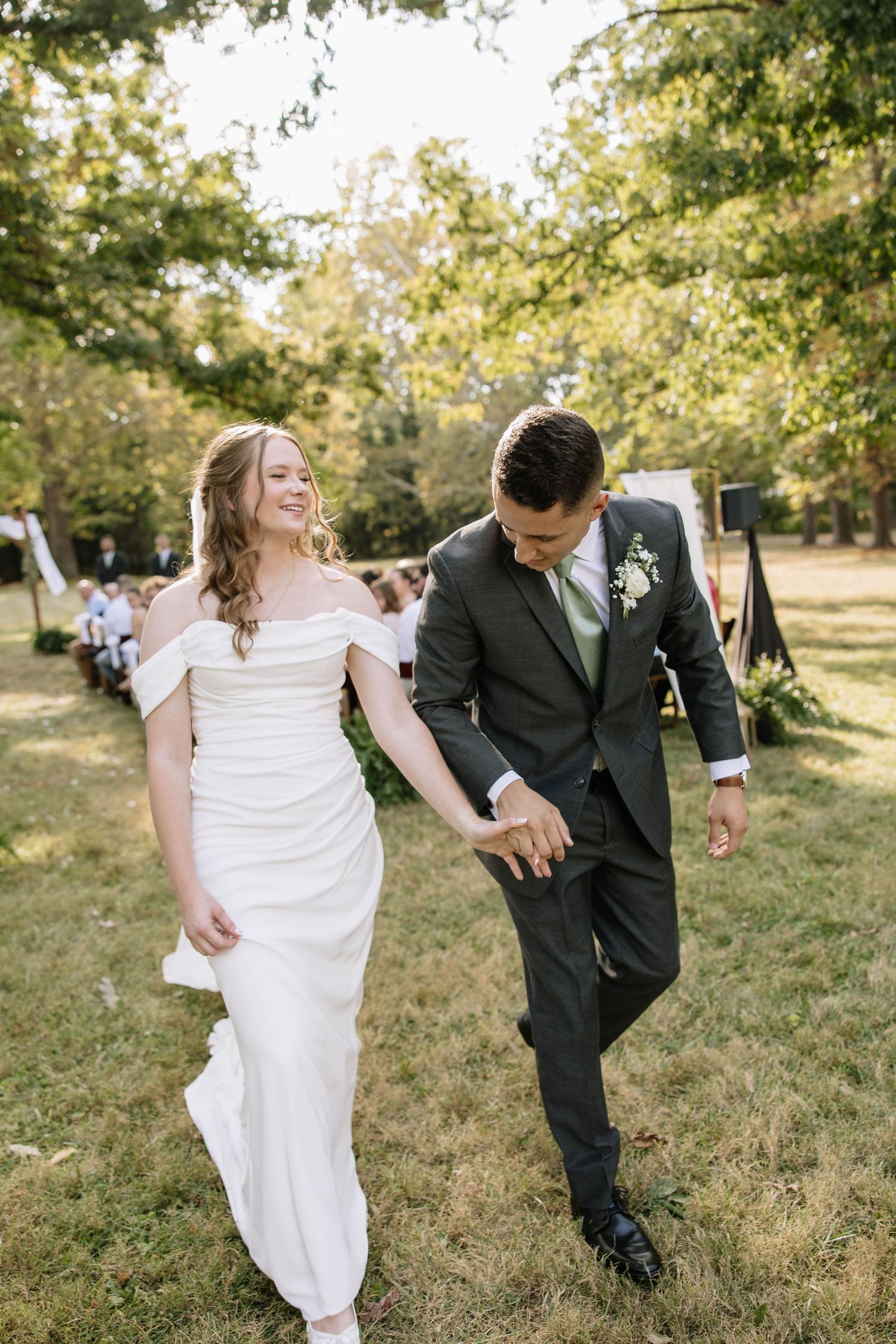 Newlyweds sharing a playful moment while walking through a grassy outdoor setting.