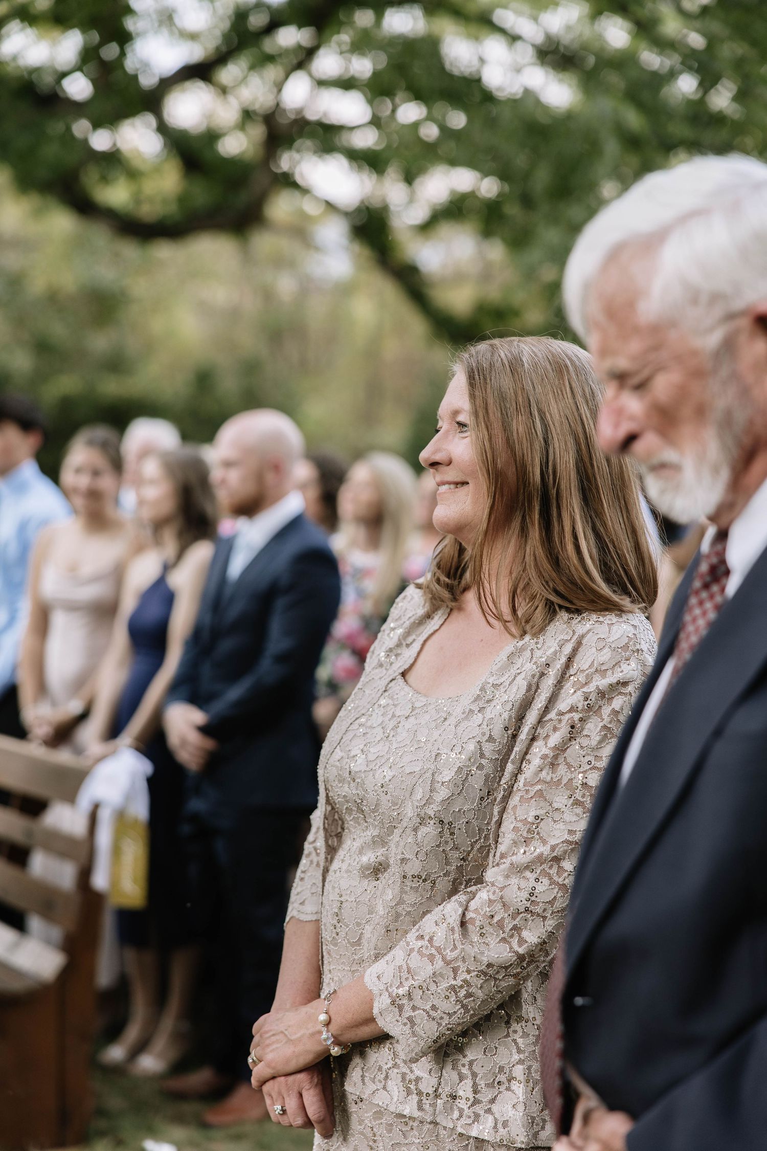Wedding attendees seated in rows of wooden chairs during an outdoor ceremony.