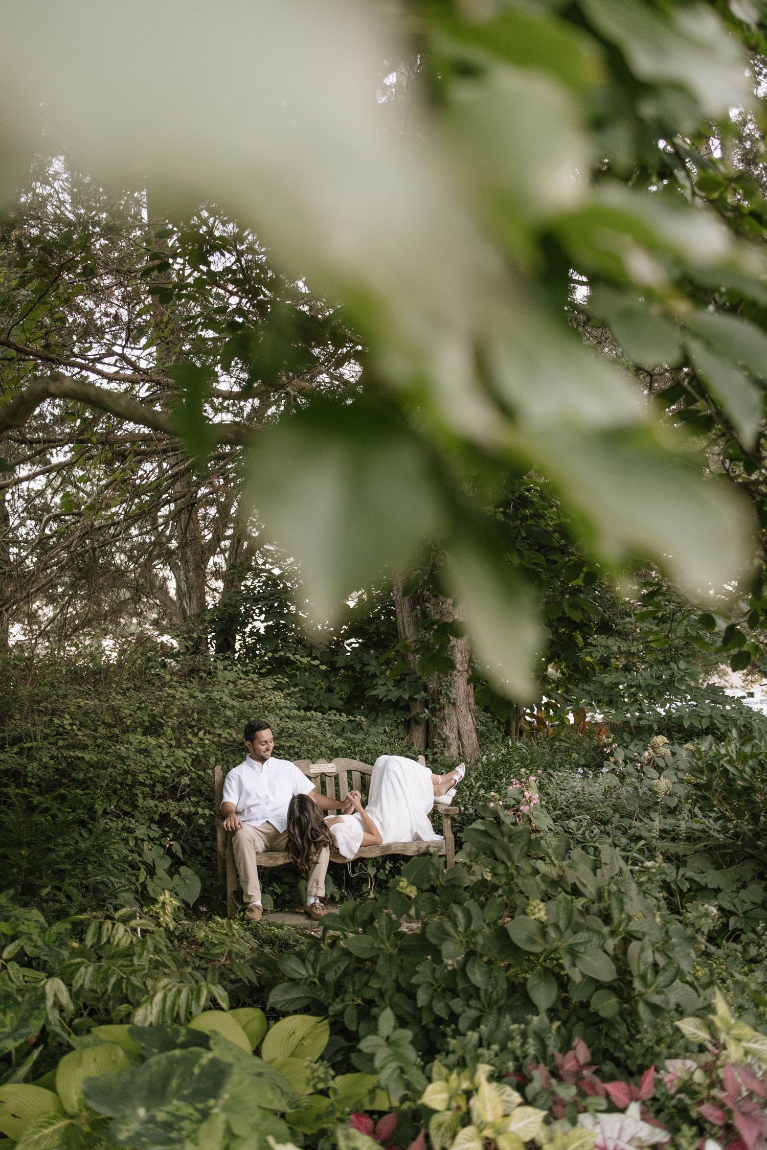 Couple photographed through foliage during outdoor garden session.