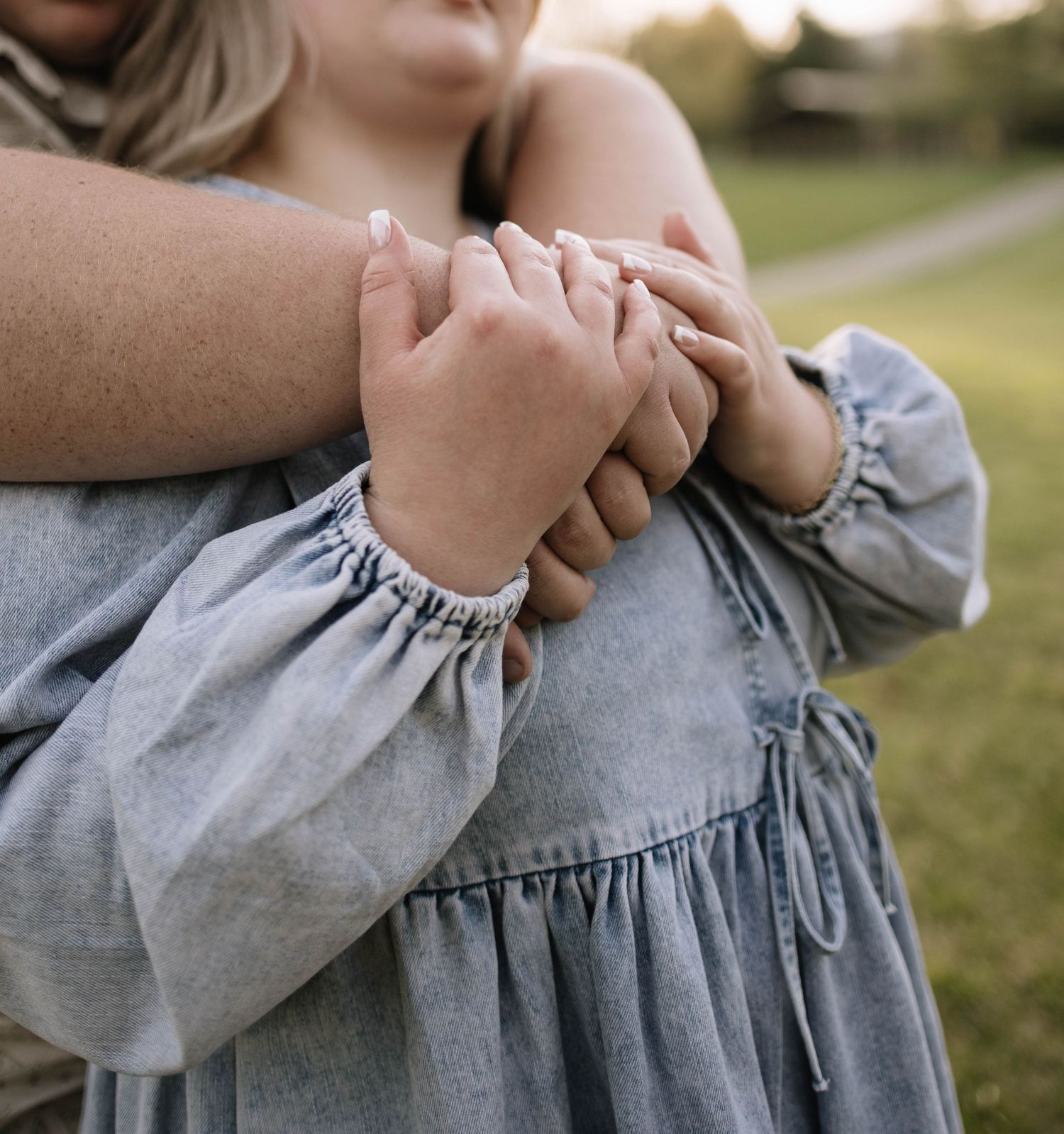 A mother and child embracing outdoors, holding hands in matching gray dresses with a bracelet visible.