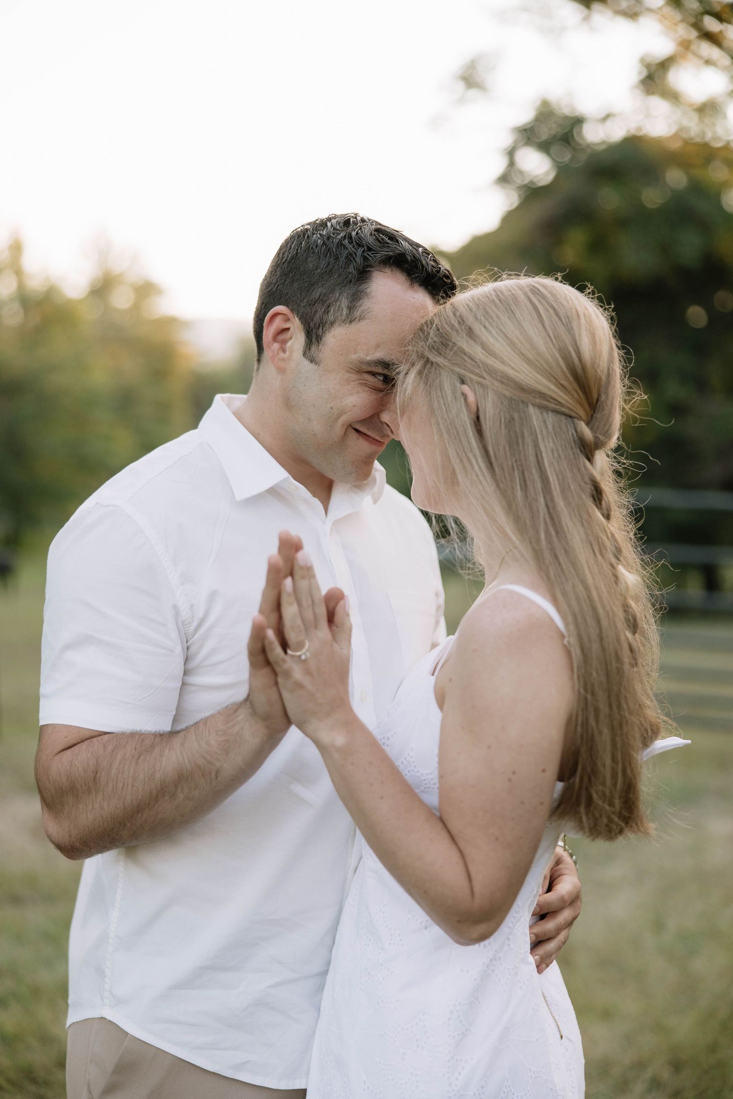 A couple in matching white outfits laughing and embracing in a sunny field.