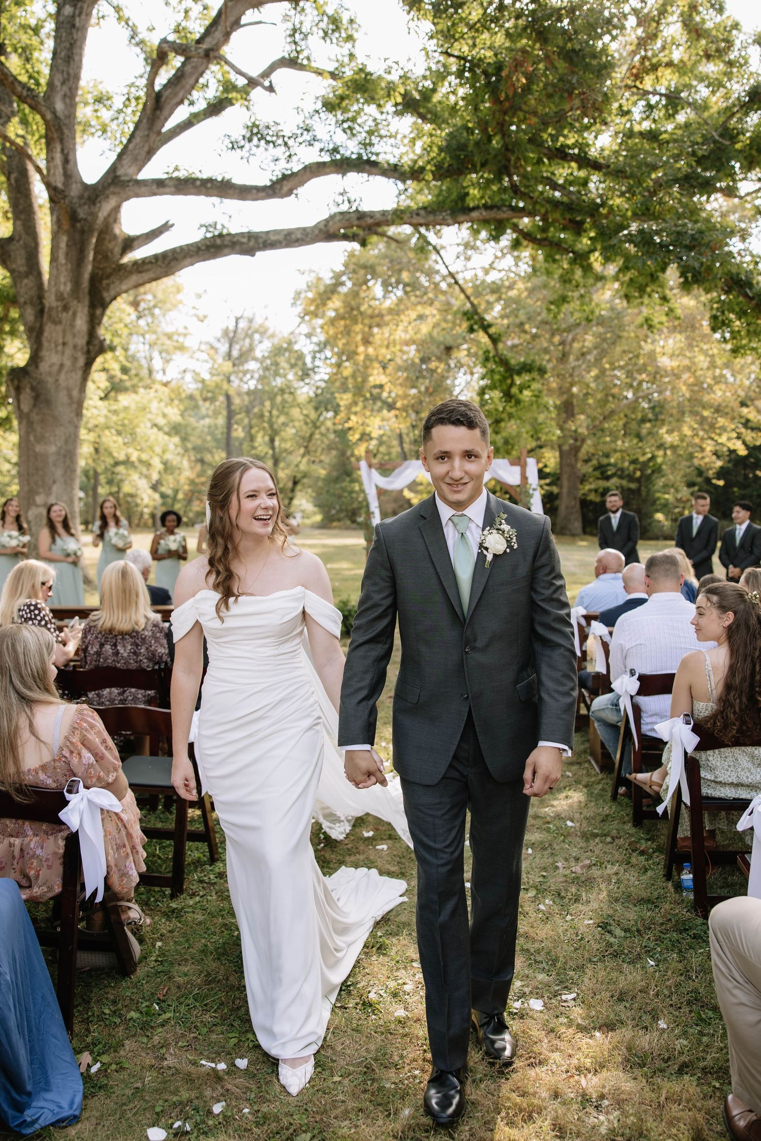 Joyful wedding couple walking together outdoors in a sunlit garden setting with guests in background.