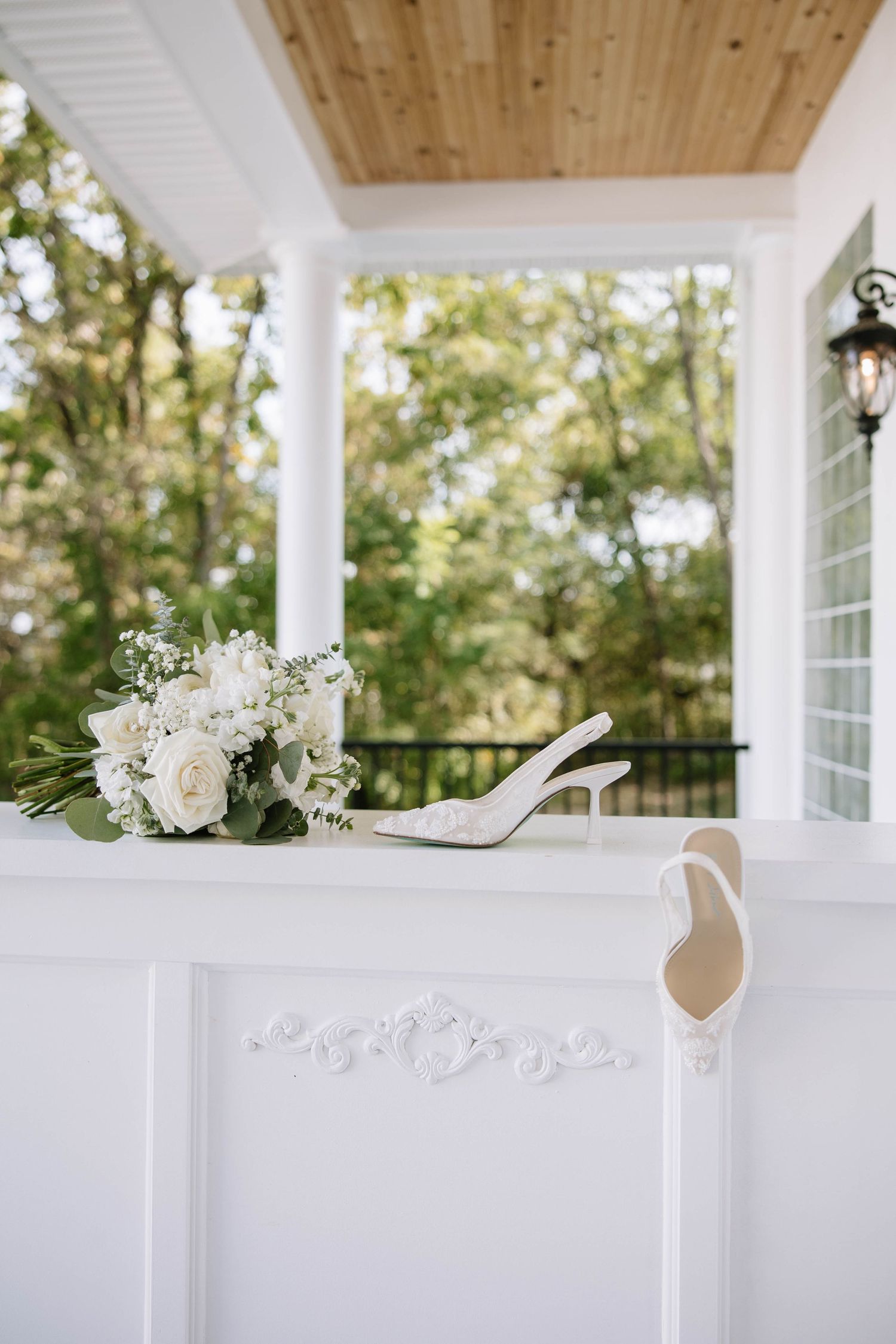 White floral arrangements on porch railing with wooden ceiling and columns.