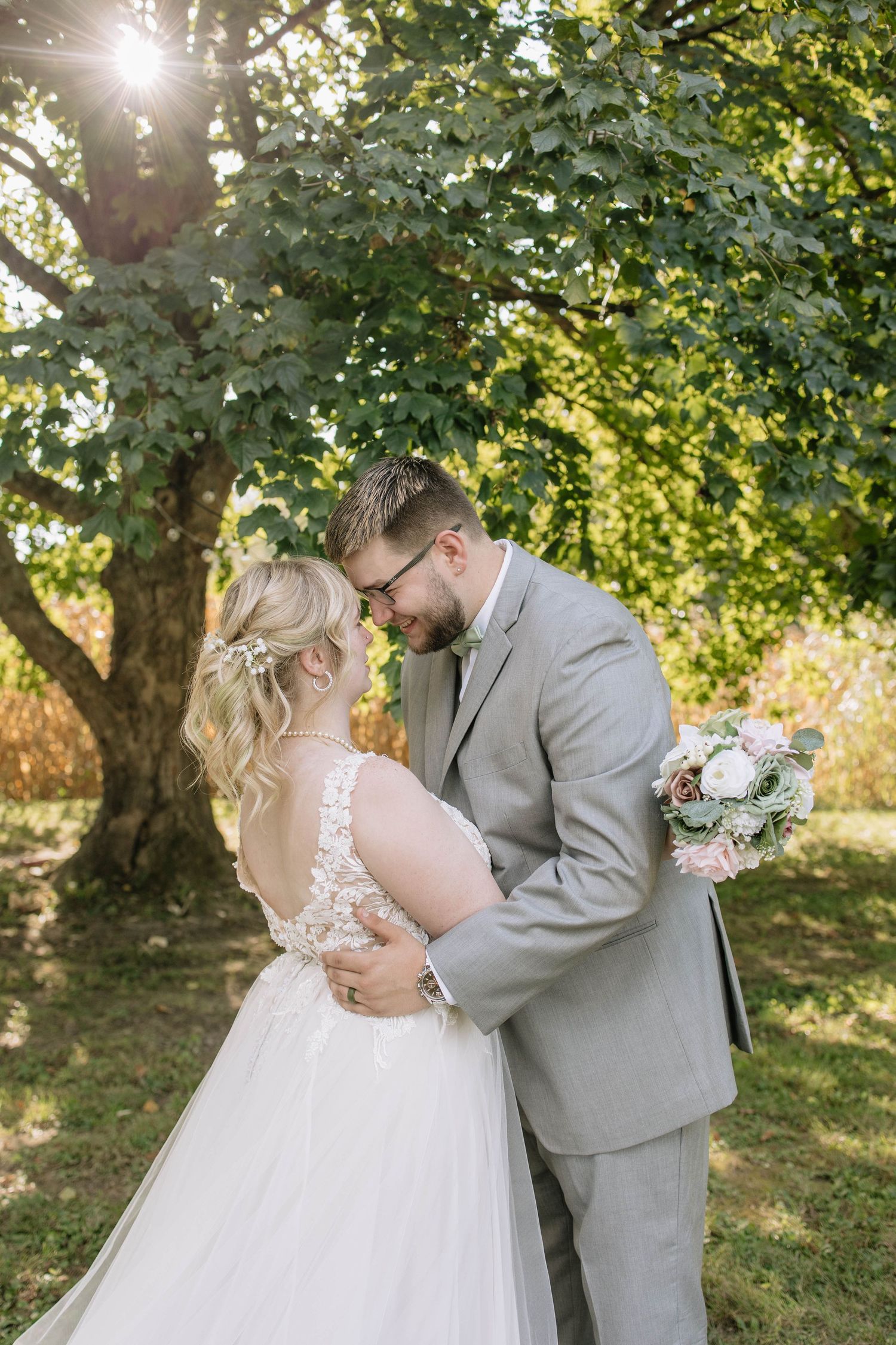 Intimate wedding couple moment captured under sunlit trees in a garden setting.